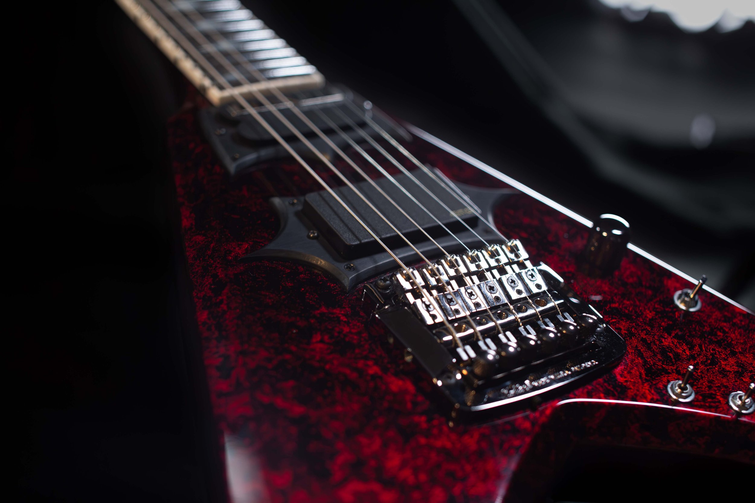 Close-up of an electric guitar with a red and black marbled finish, focusing on the strings and bridge.