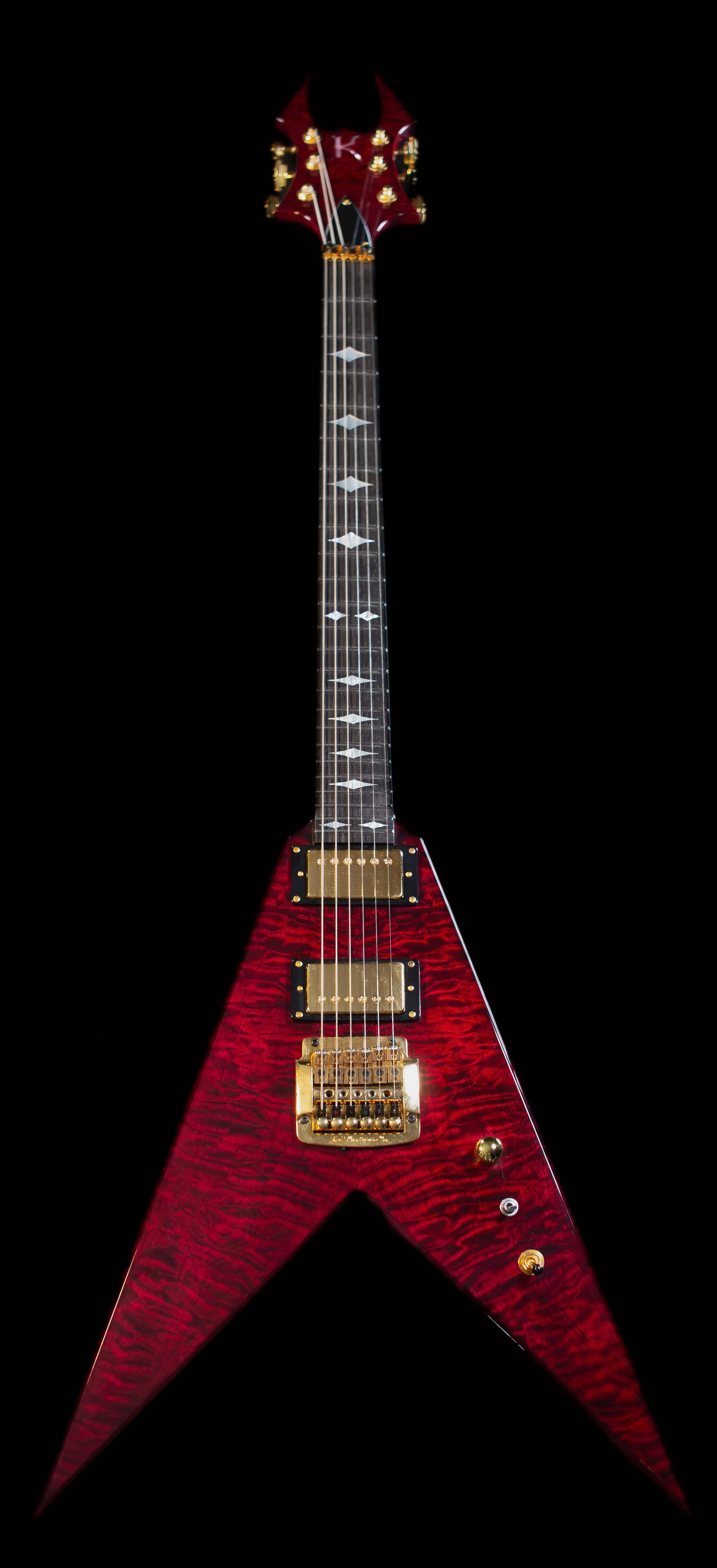 Red electric guitar with a star-shaped body, black pickguard, gold hardware, and diamond inlay fret markers on a black background.