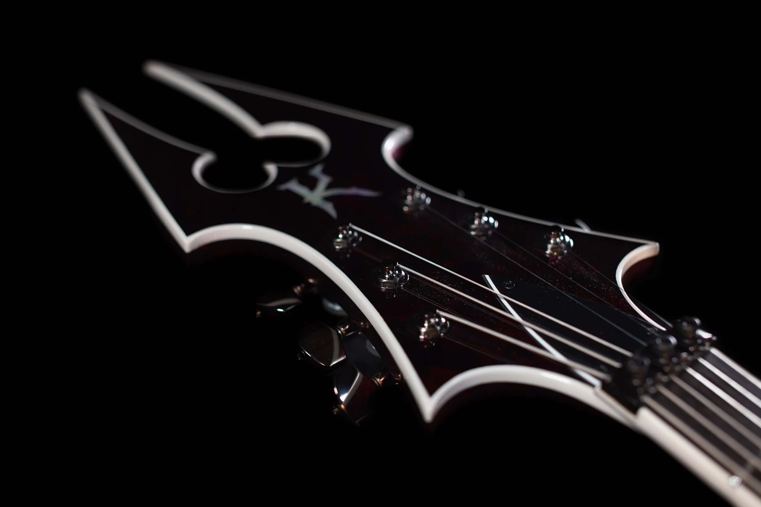 Close-up of an electric guitar fretboard with strings and tuning pegs, set against a dark background.