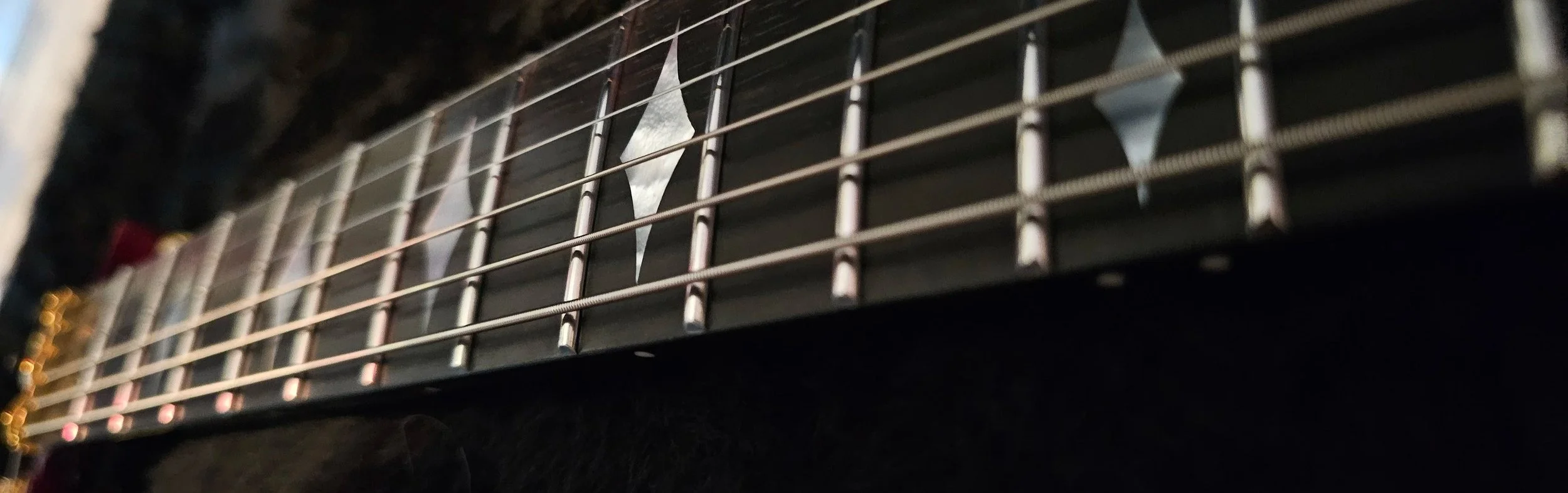 Close-up of an electric guitar's fretboard with metal frets and mother of pearl inlays.
