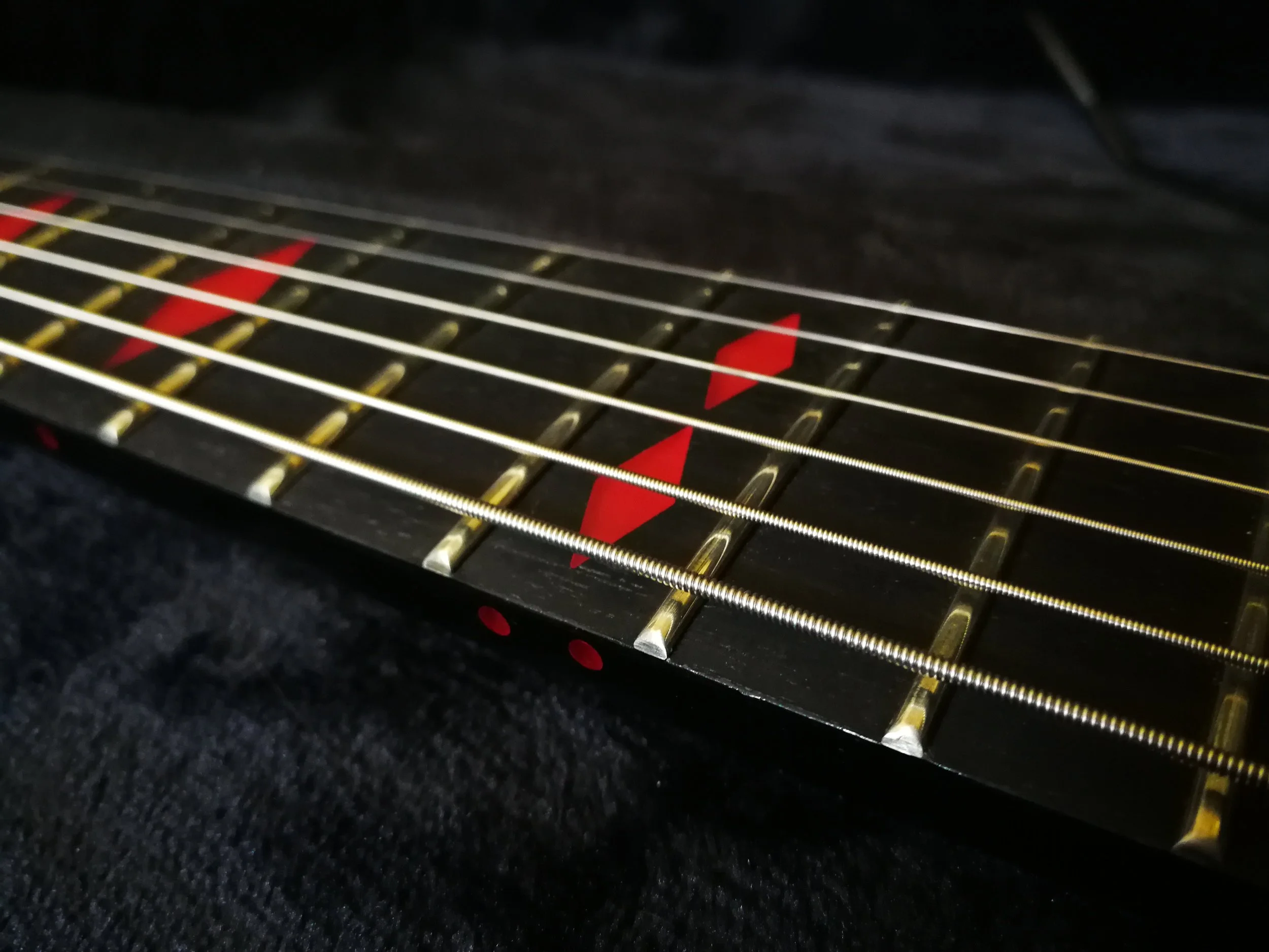 Close-up of an electric guitar neck with strings and fret markers. The fret markers are red diamond shapes on a black ebony fretboard.