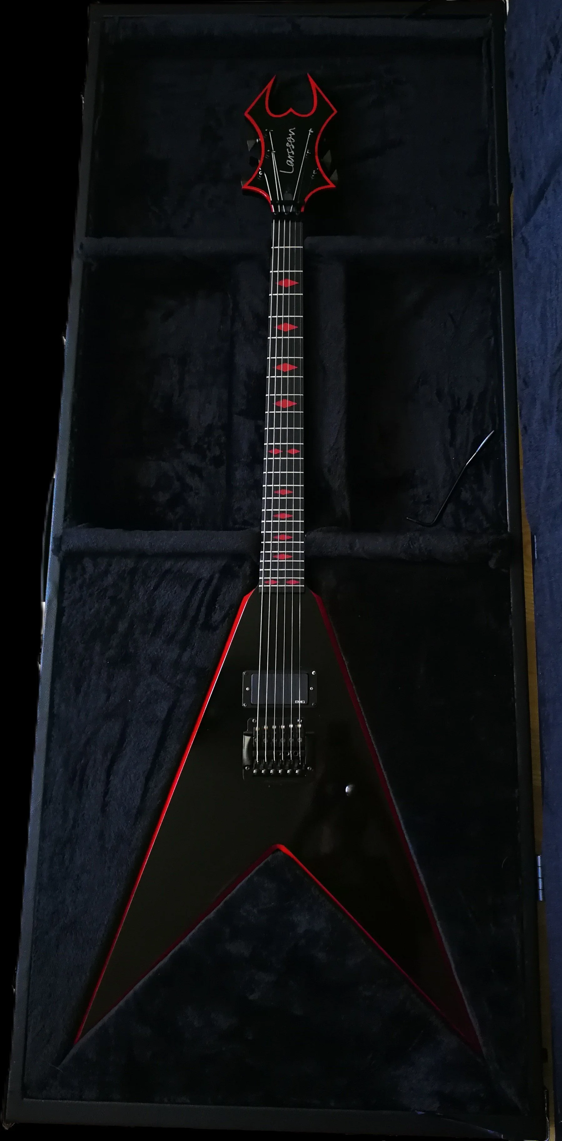Black electric guitar with red accents and sharp angular design, placed inside a black hard case with plush lining.