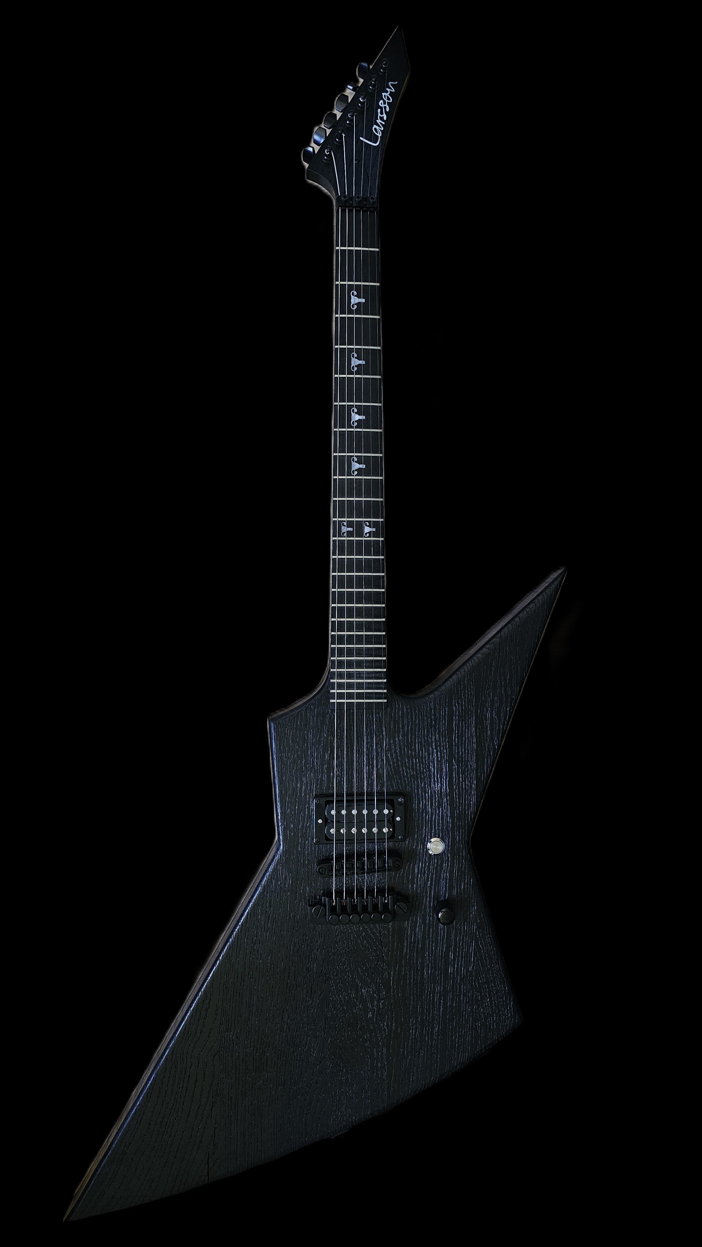 Black electric guitar with an angular, modern design, six strings, and a signature on the headstock, set against a black background. Made out of oak or a rustic look.