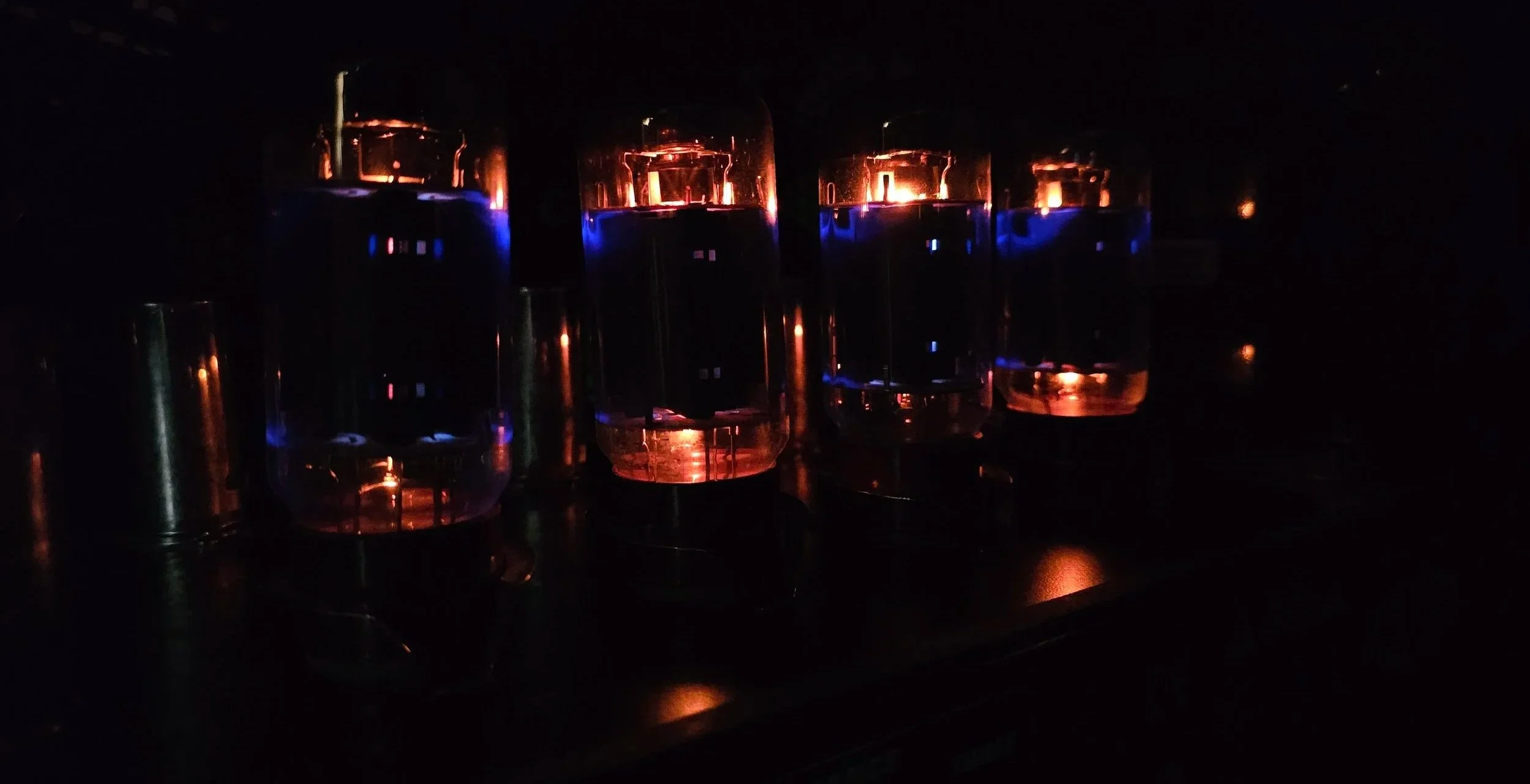 Close-up of glowing glass vacuum tube lights with orange and blue reflections in a dark environment.
