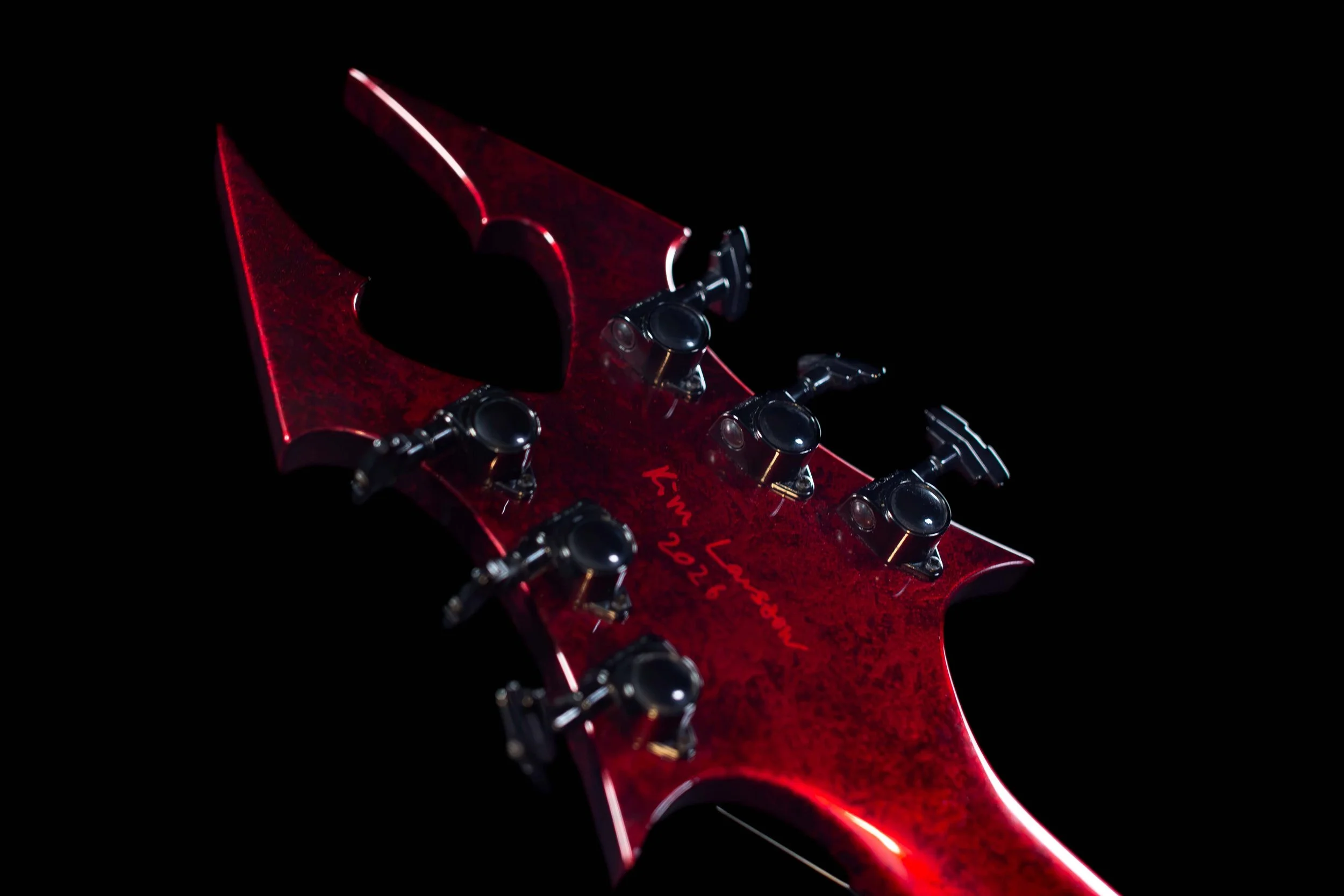 Close-up of a red electric guitar's aggressive headstock with tuning pegs.