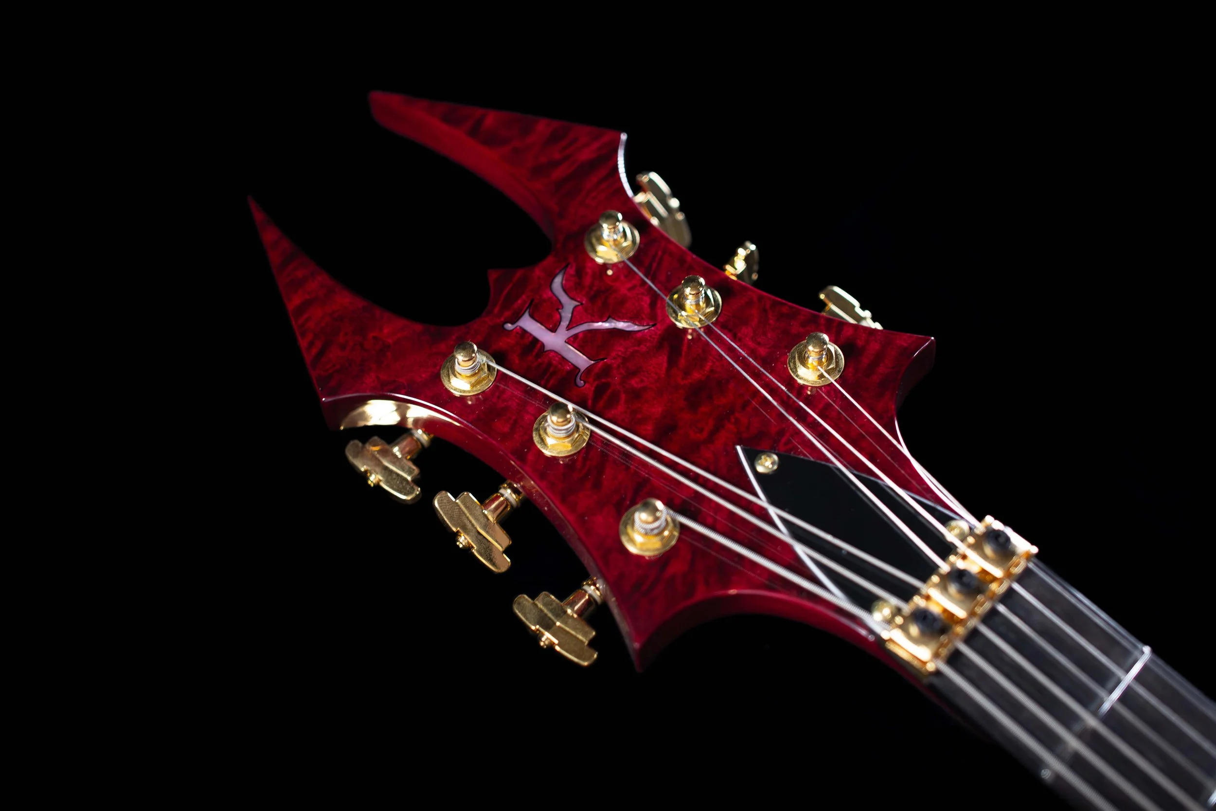 Close-up of a red and black electric guitar headstock with gold tuning pegs and a logo on the front.