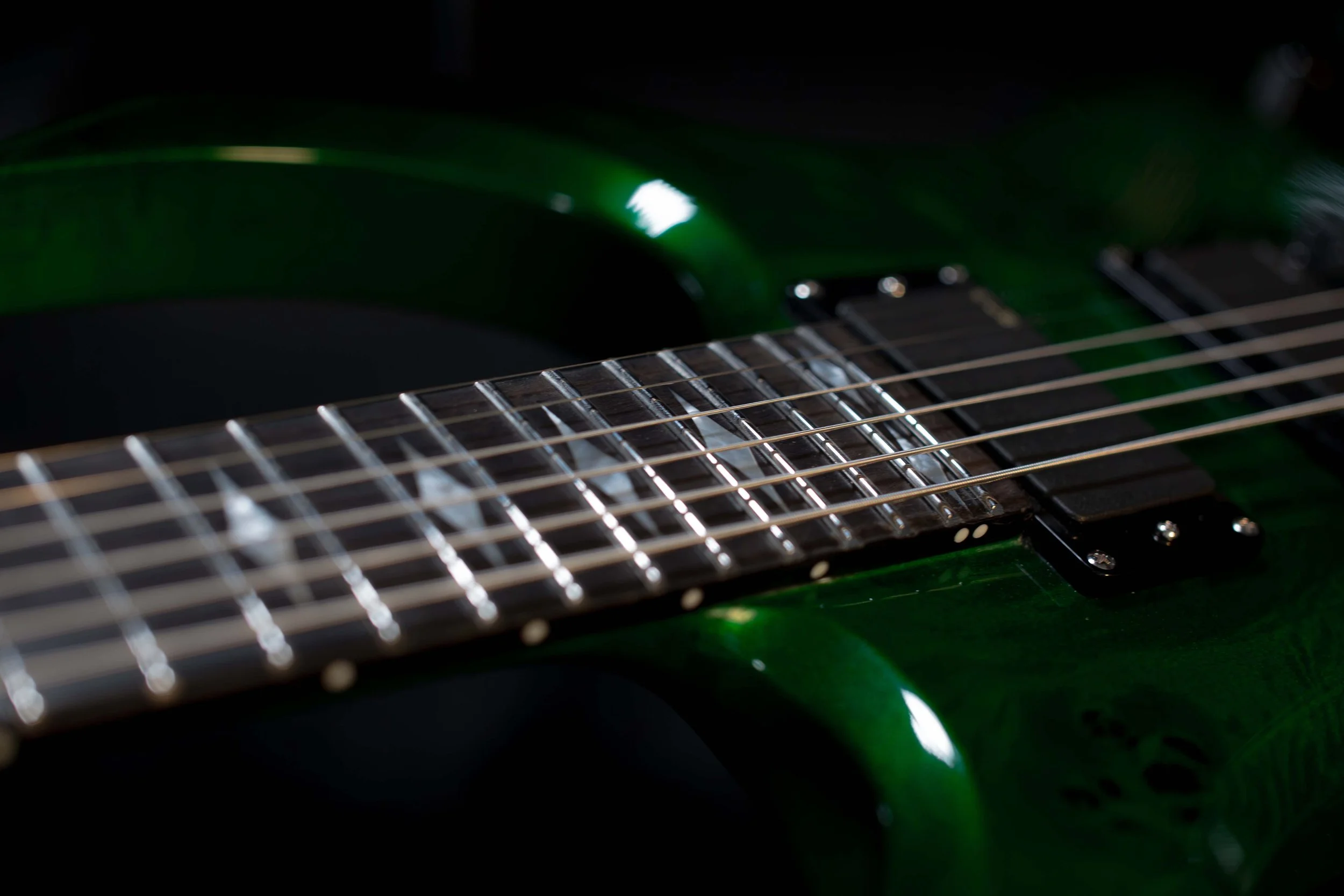 Close-up of an electric guitar with green body, focus on the fretboard and strings.