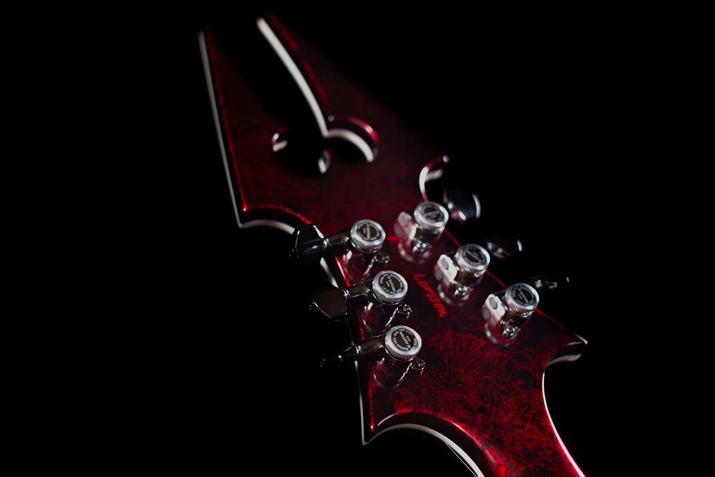 Close-up of a red electric guitar neck with tuning pegs and knobs visible, set against a black background.