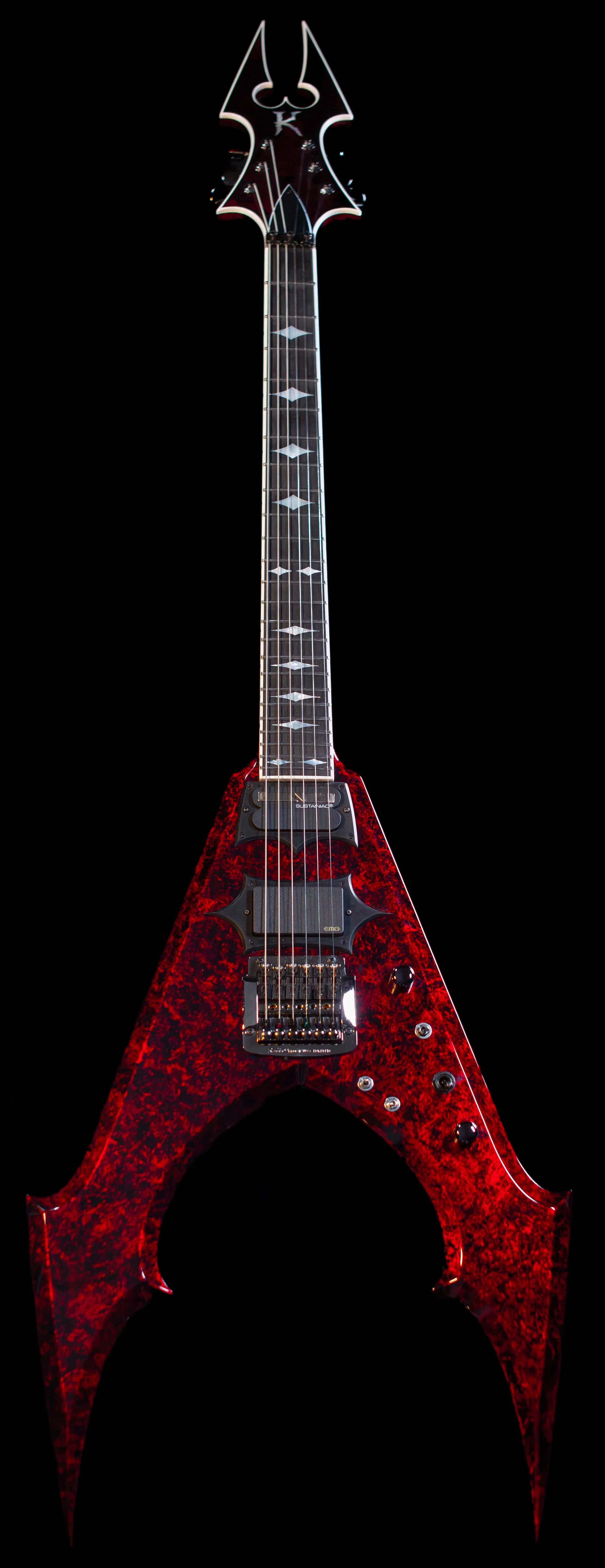 A red electric guitar with a pointed, aggressive body shape, black pickups, and intricate fret inlays, set against a black background.