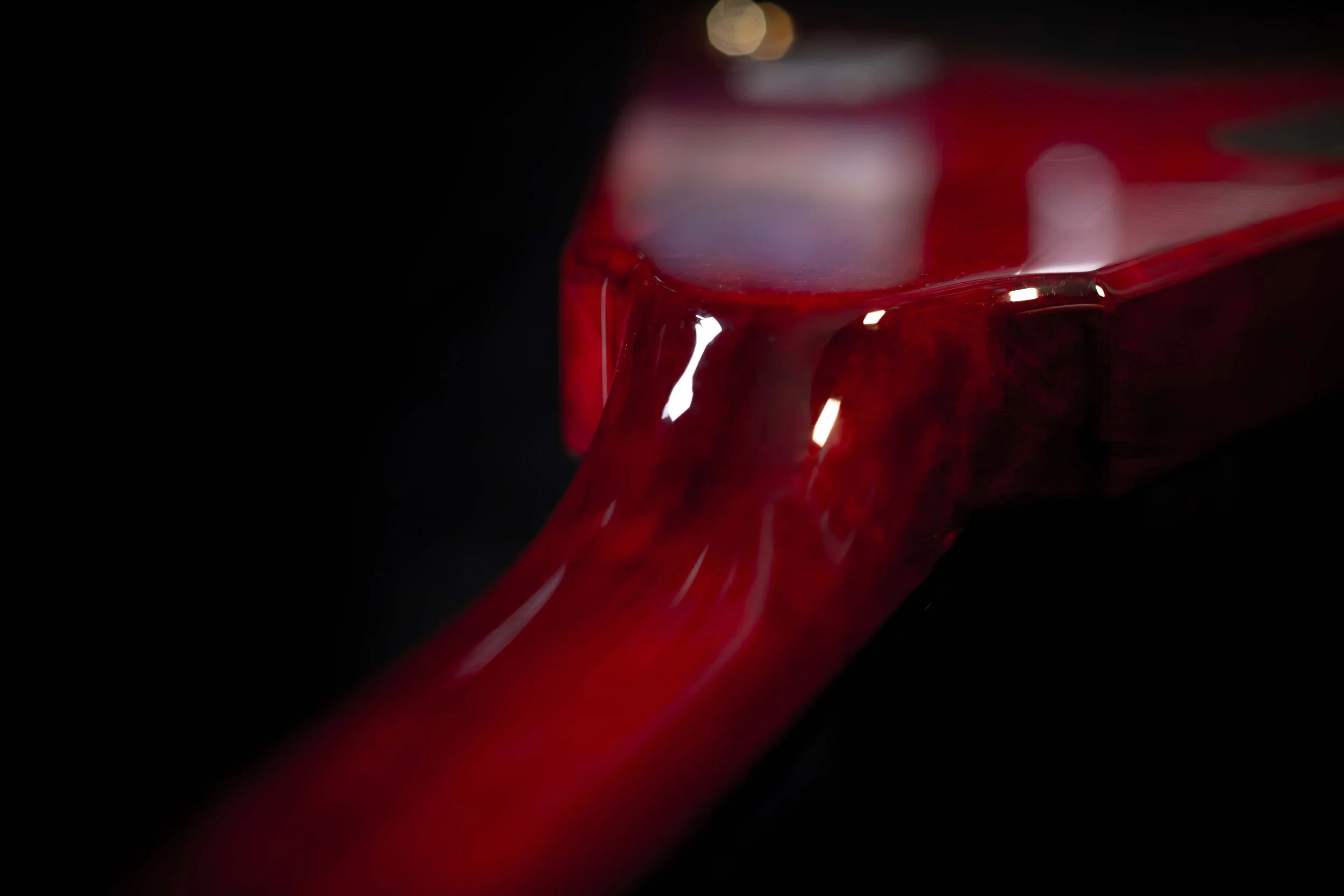 Close-up of red liquid flowing over a surface, with dark background and reflections.