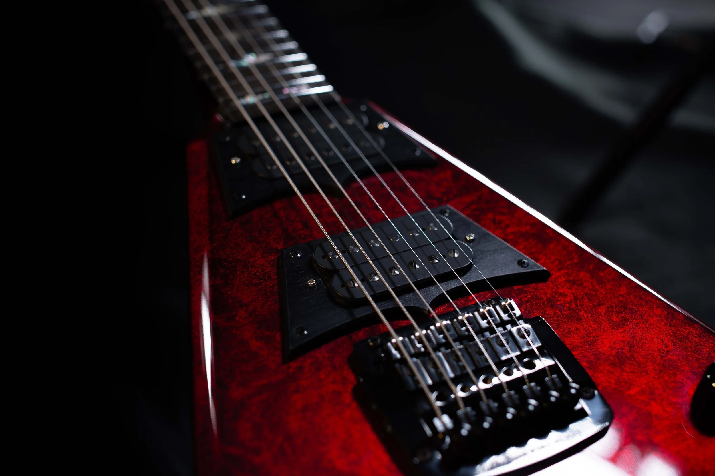 Close-up of an electric guitar's neck and body with a unique red finish, showing strings, pickups, and fretboard. Kahler bridge.