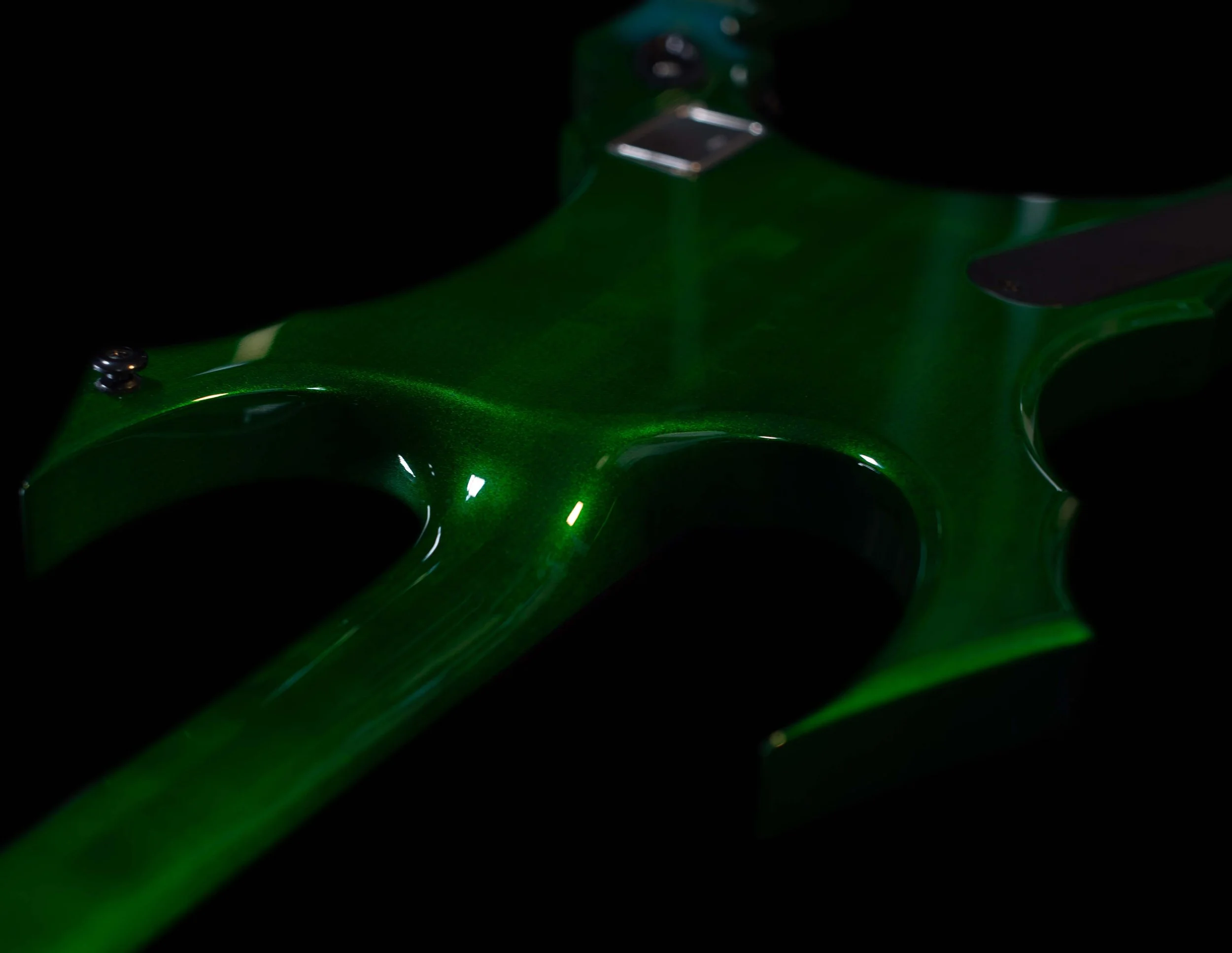 Close-up of a green electric guitar with a perfect neck-through construction, partially visible, with a dark background.