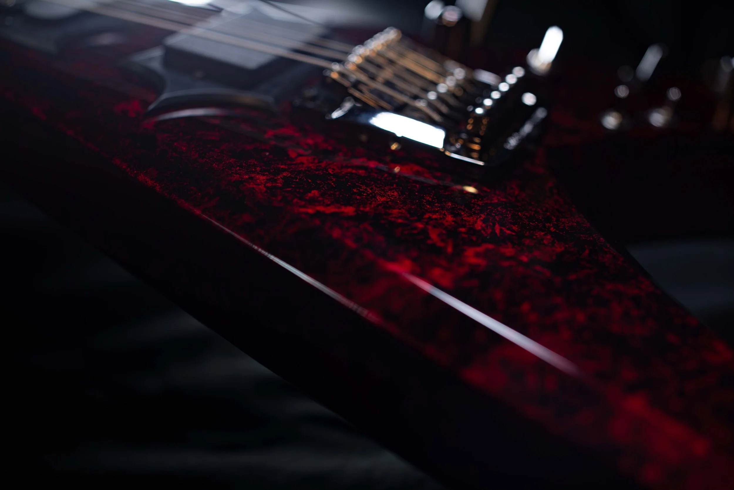 Close-up of a dark, reflective surface with patches of red, possibly a car with a red paint job, illuminated by light.