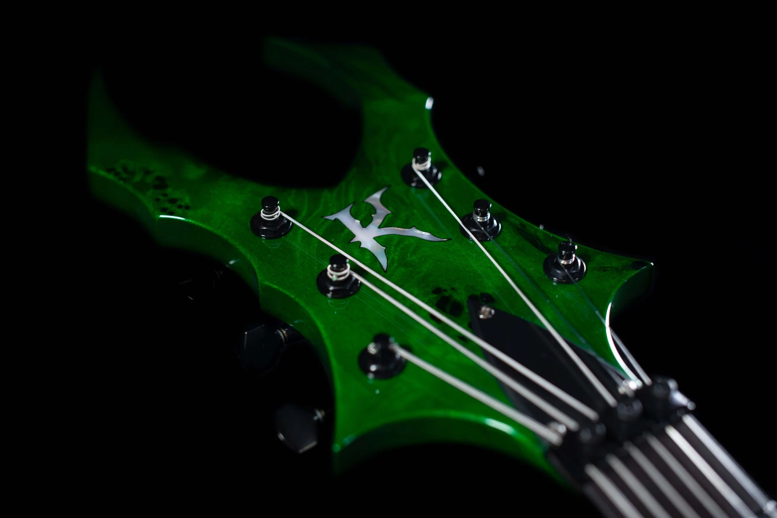 Close-up of a green electric guitar headstock with black tuning pegs and a skull logo.