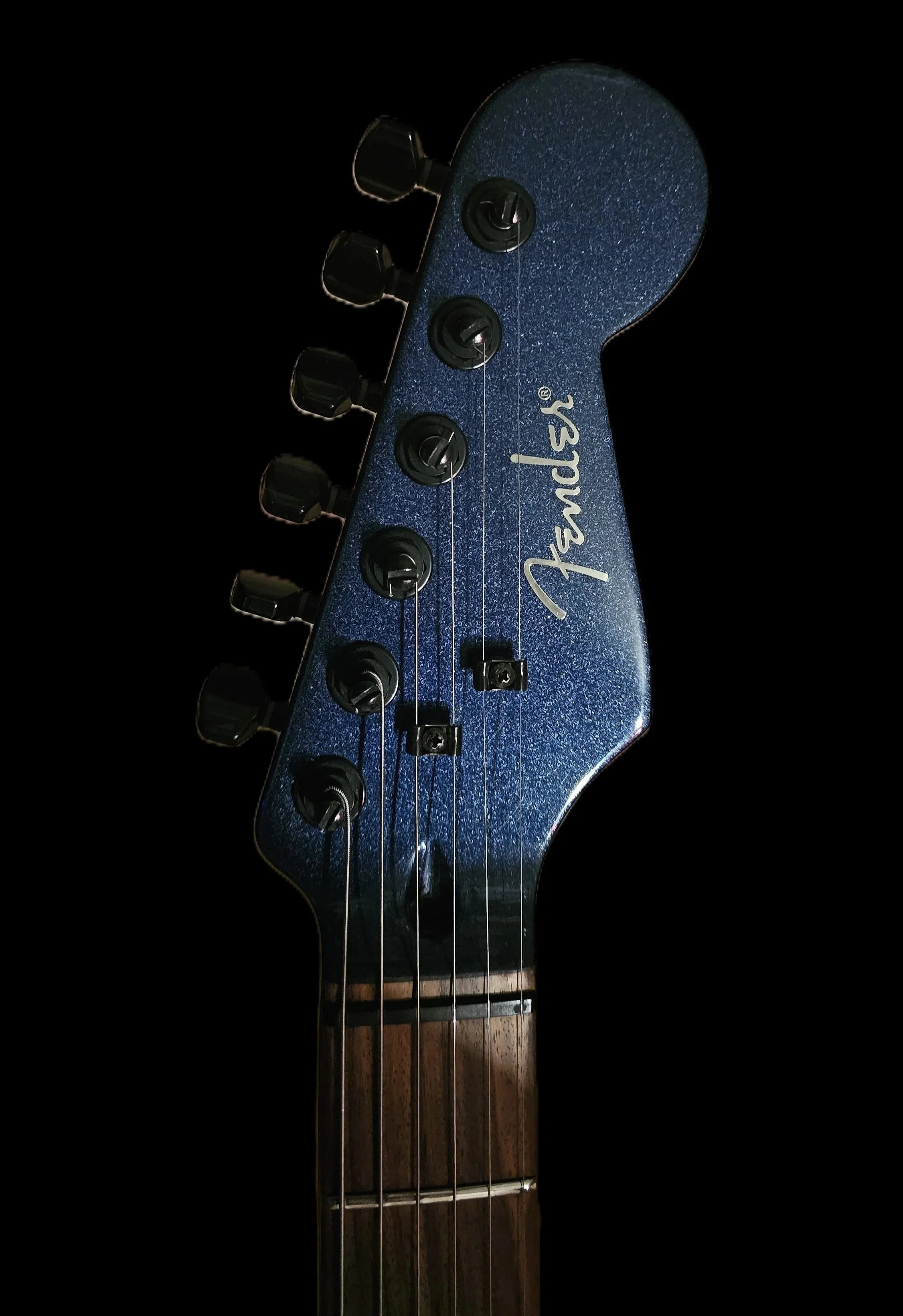 Close-up of a Fender electric guitar headstock with tuning pegs, strings, and logo, against a black background.