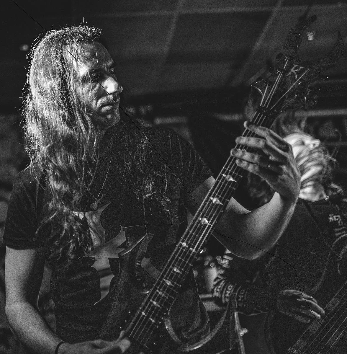 A black and white photo of a man with long, wavy hair playing an electric guitar, focused and immersed in music.