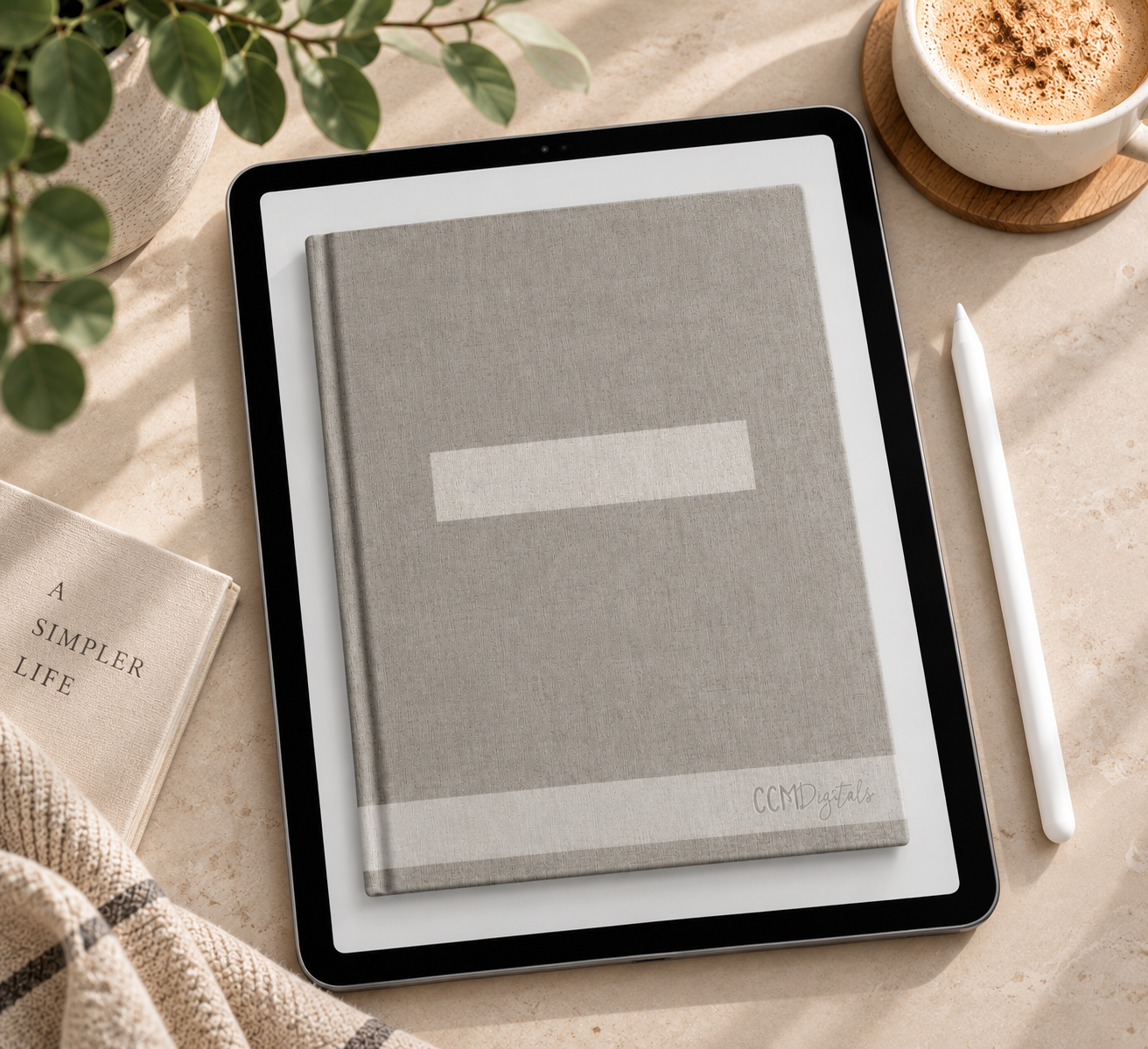 A flat lay of a workspace with a tablet displaying a closed gray book, a white stylus, a beige book titled 'A Simpler Life', a cup of frothy coffee on a wooden coaster, and a potted plant on a beige marble surface.