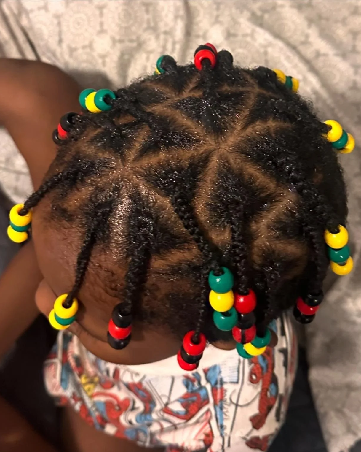 Close-up of a child's head with small twisted braids decorated with colorful beads in red, yellow, green, and black.