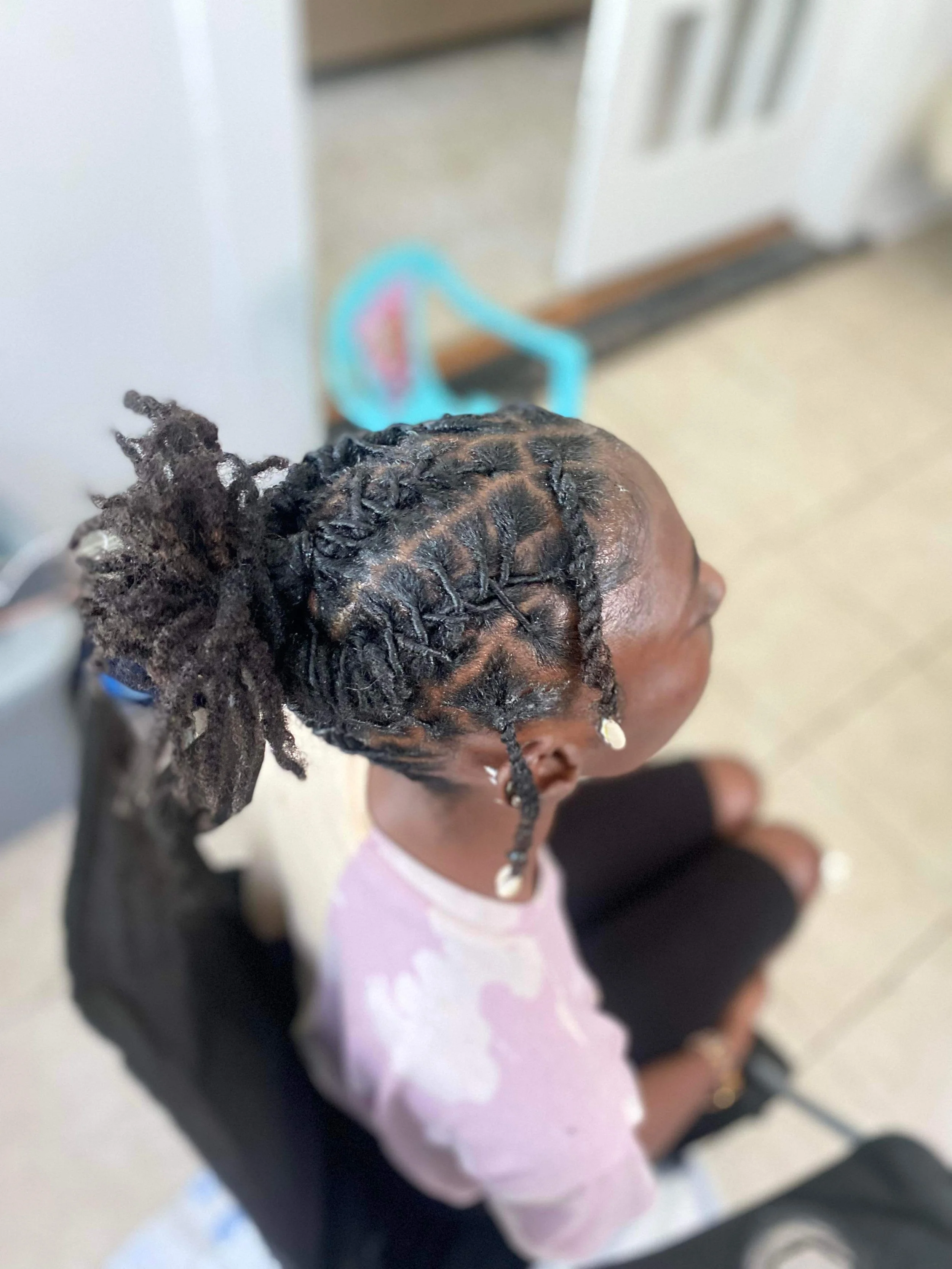 Close-up of a person with styled, coiled dreadlocks sitting in a waiting area, possibly at a salon.