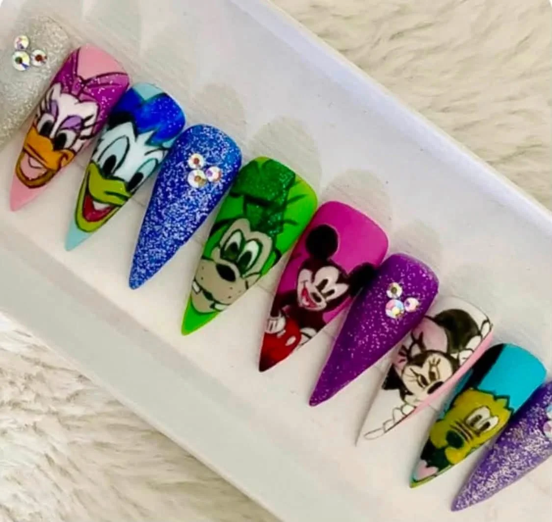 Colorful, cartoon-themed nail designs featuring Mickey Mouse, Minnie Mouse, Donald Duck, Daisy Duck, and Goofy, with glitter and rhinestone accents.
