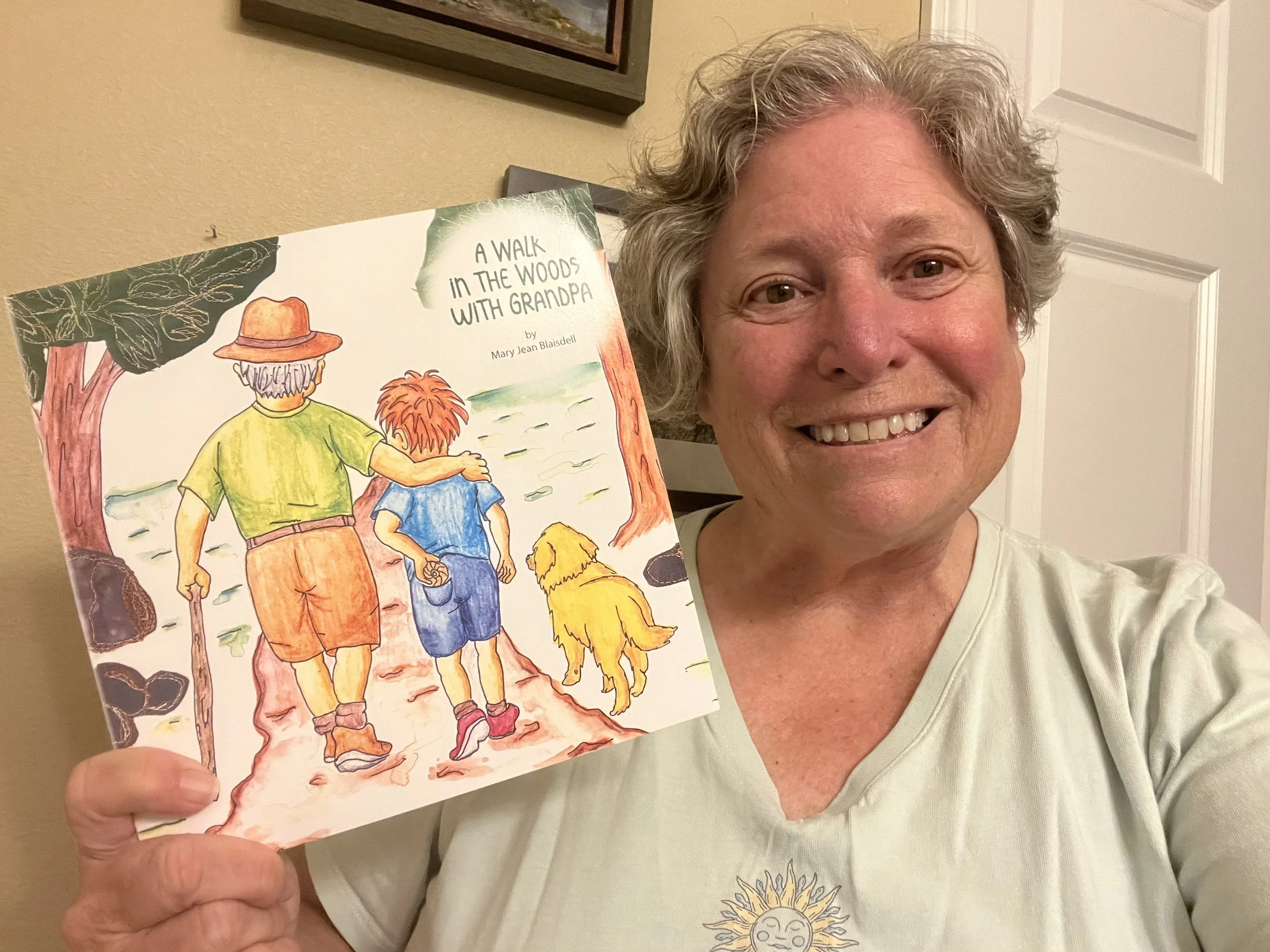 A picture of author, Mary Jean Blaisdell holding a book called "A Walk in the Woods with Grandpa"
