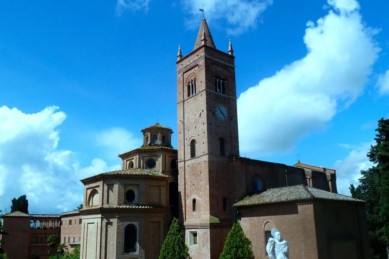 A historic brick church with a tall clock tower and a statue in front, set against a blue sky with clouds.