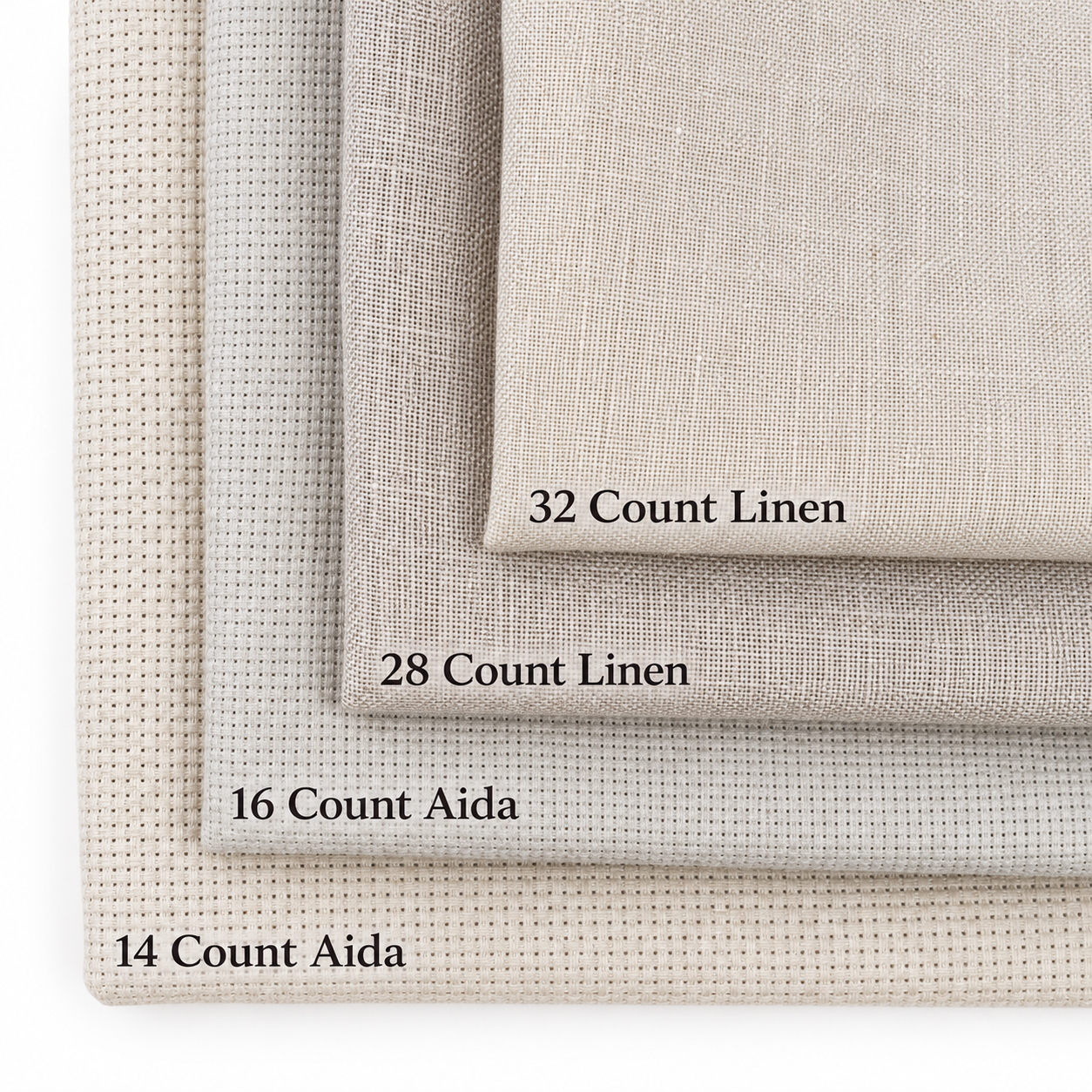 Four stacks of linen fabrics labeled with thread counts: 32 Count Linen, 28 Count Linen, 16 Count Aida, and 14 Count Aida, in neutral colors with different textures.
