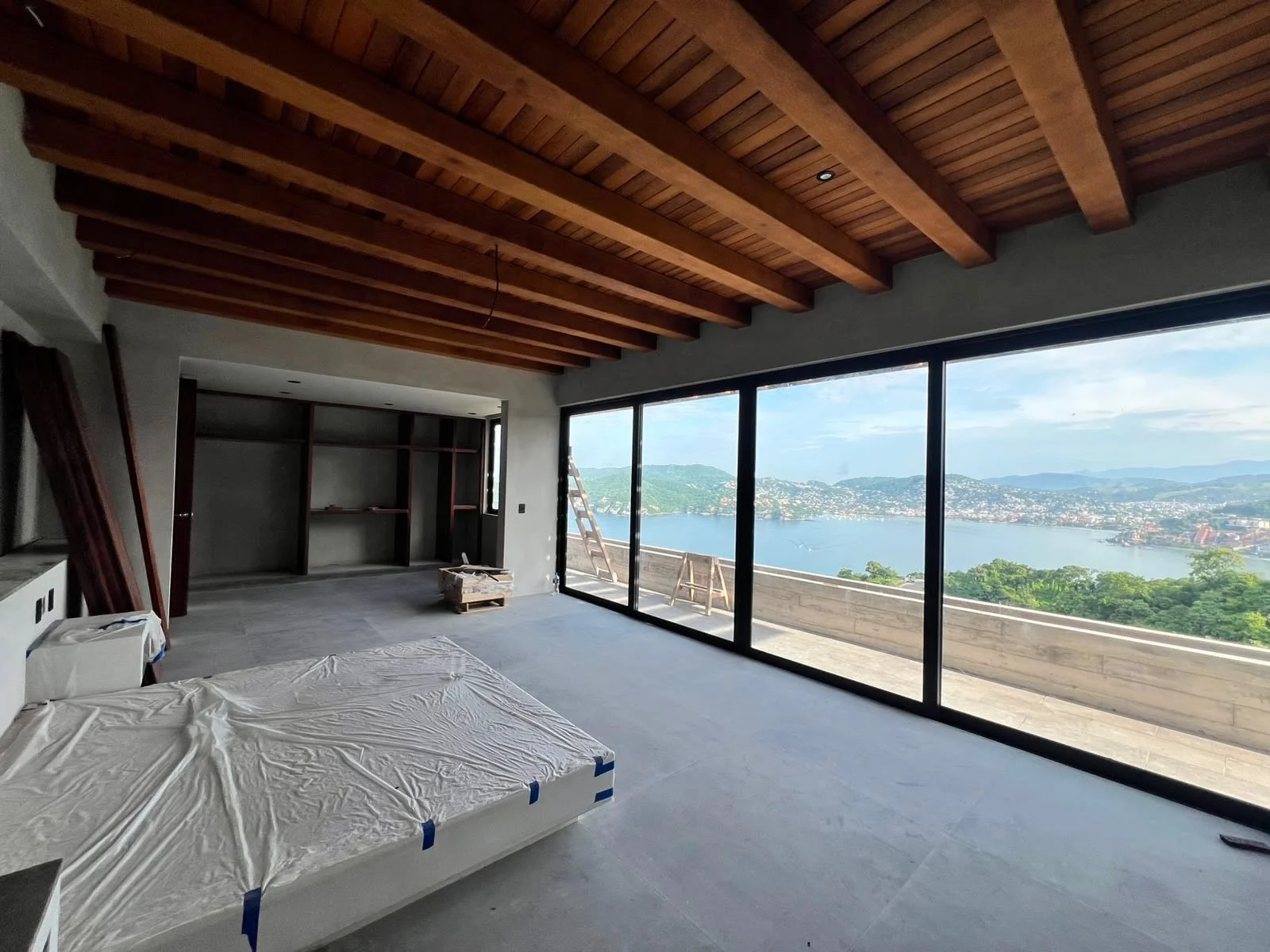 Interior of a house under construction with large glass sliding doors opening to a view of a river and mountains.