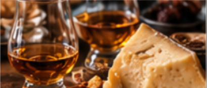 Two glasses of whiskey and a wedge of cheese on a wooden board surrounded by small bowls of snacks.