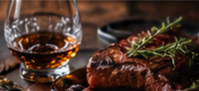 A glass of whiskey and a cooked steak garnished with rosemary.