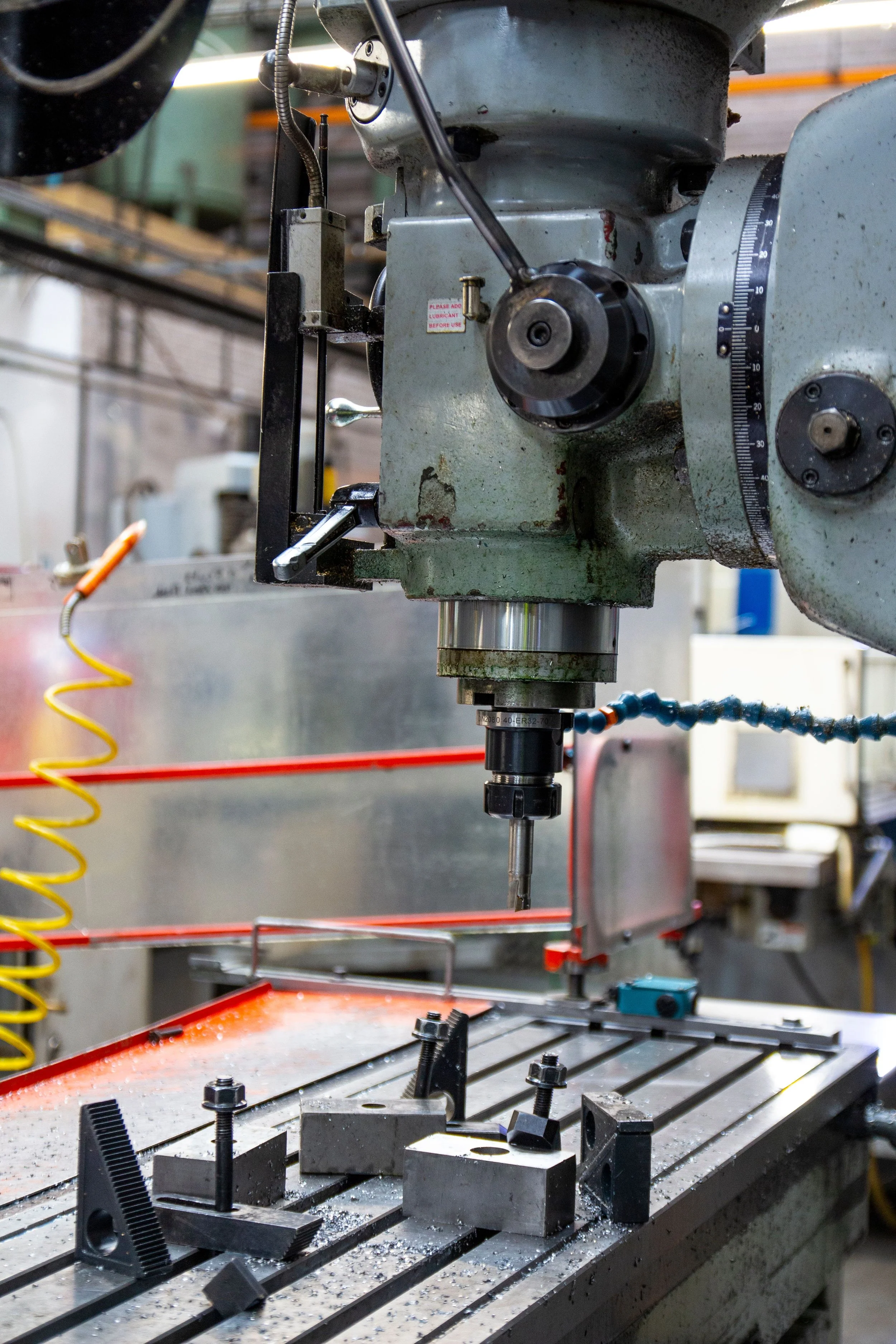 Close-up of a milling machine in a workshop, with metal parts and drills on its surface, and tool fixtures secured on the machine bed.