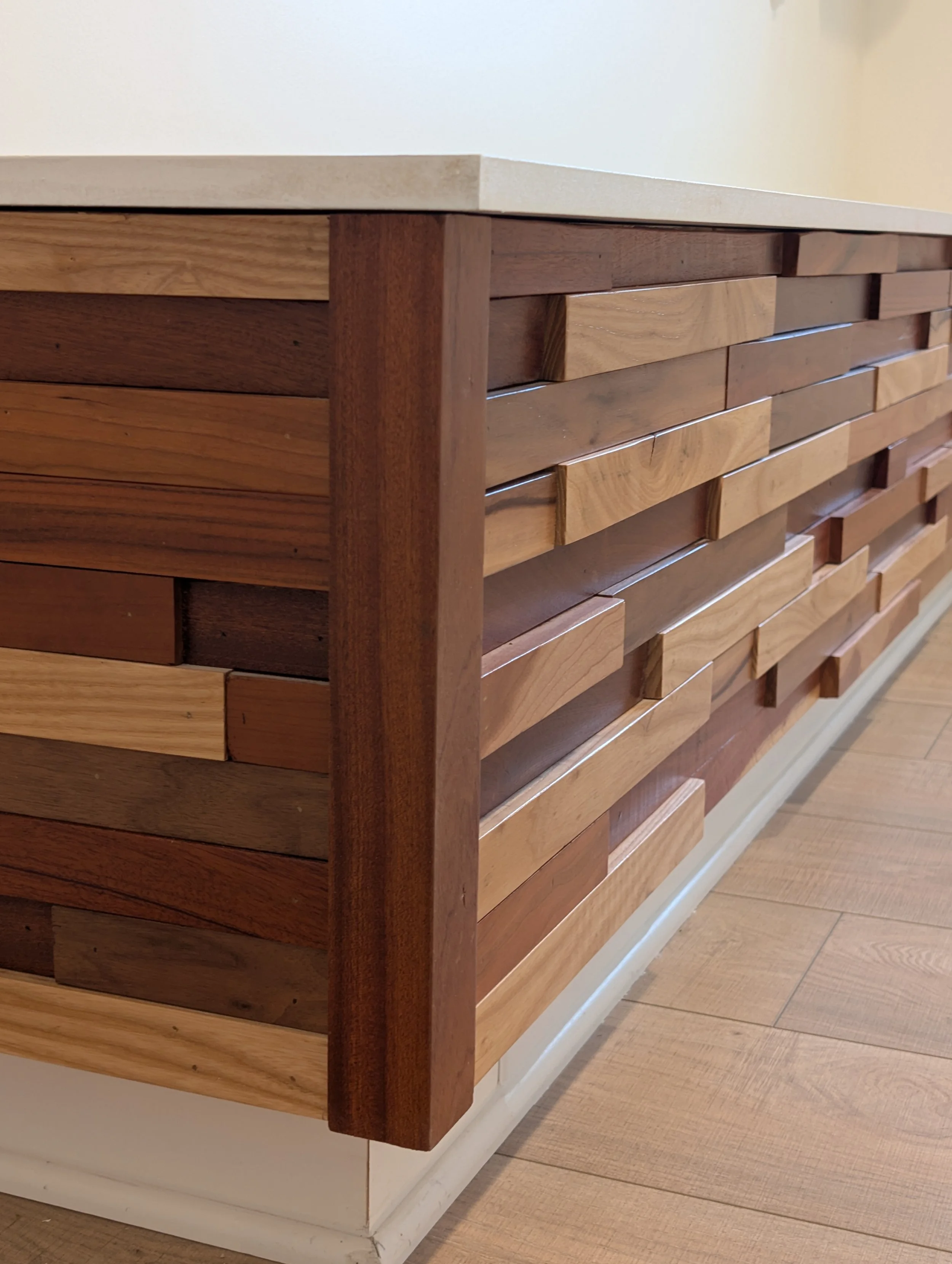Close-up view of a wooden cabinet with horizontal wood planks, standing on a white base, next to a wood floor.