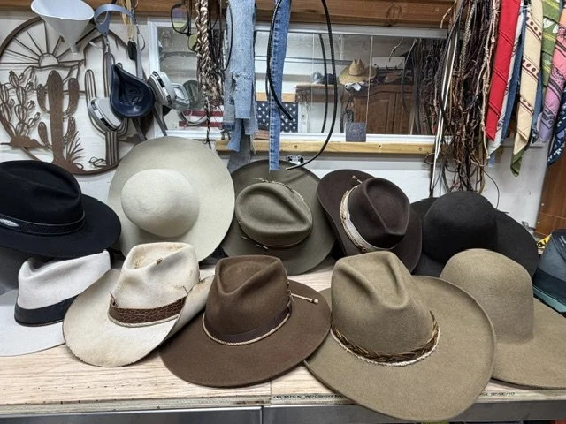 Display of various hats and headbands on a retail store counter, including fedoras, wide-brim hats, and headbands, with some headphones hanging on the wall behind them.