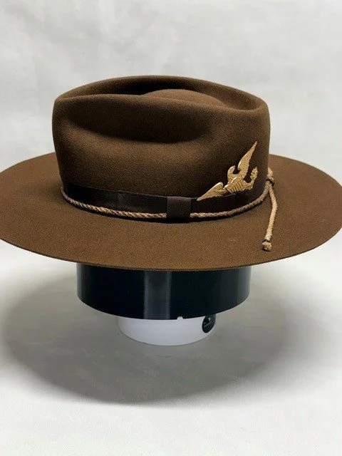 Brown campaign hat with a black band and a gold embroidered bird, placed on a black and white circular object.