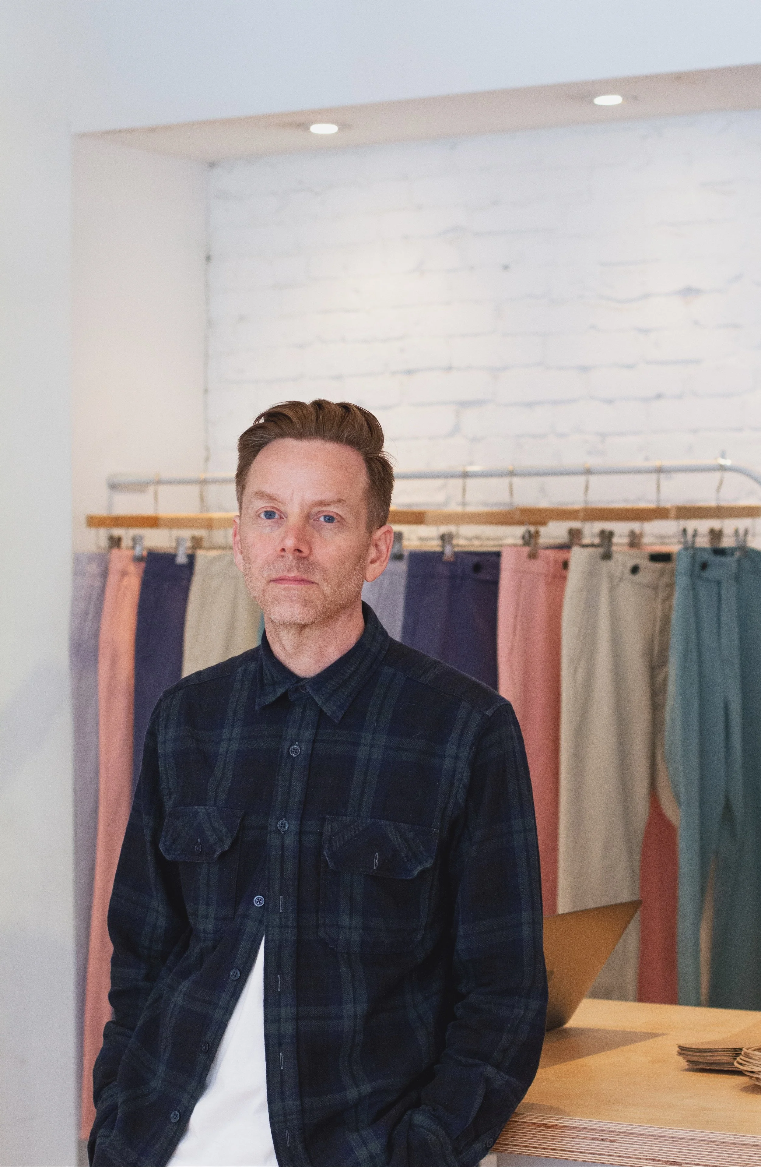 A man standing against a table with colorful clothing behind him.