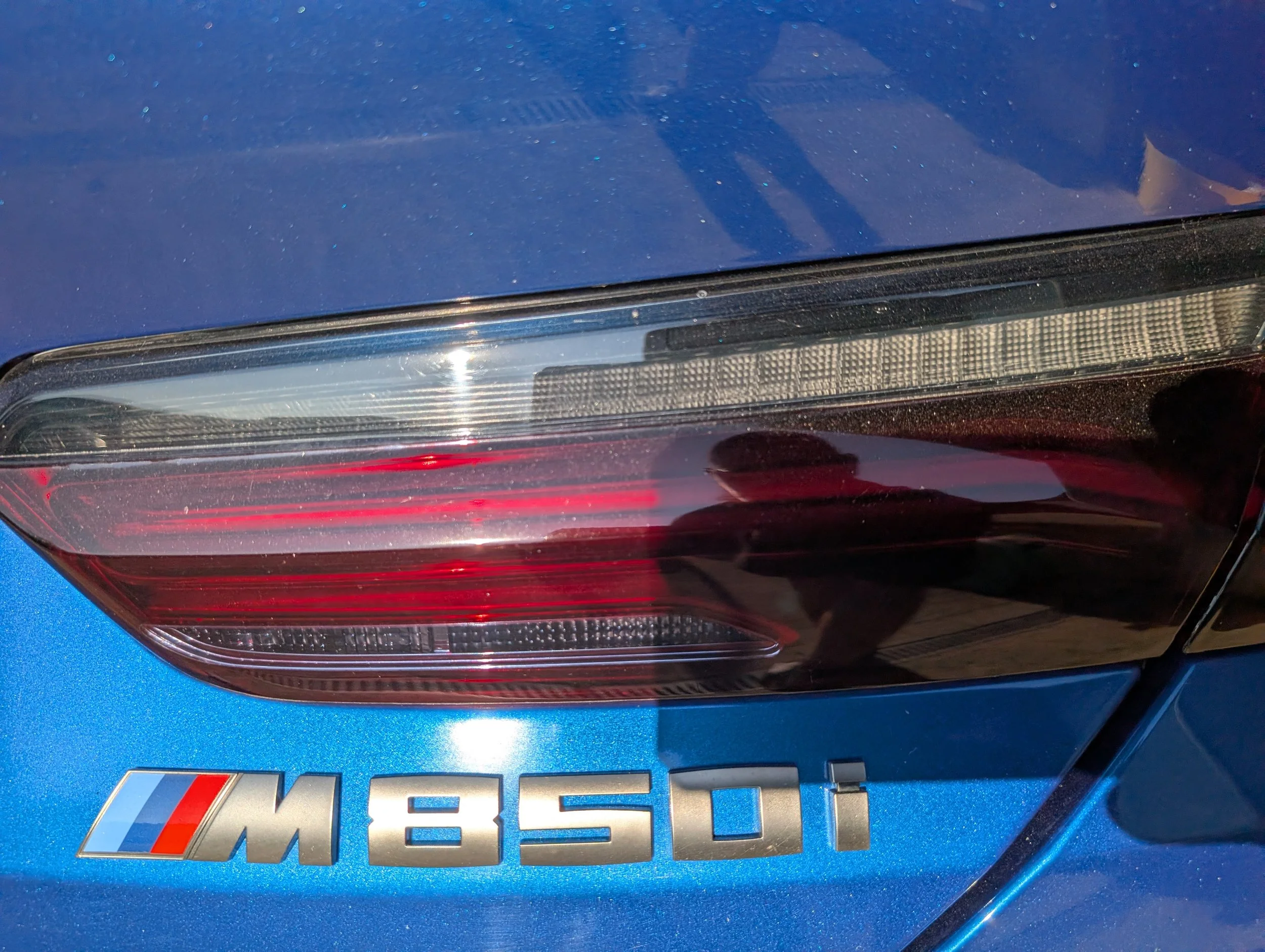 Close-up of the rear end of a blue BMW M850i car, focusing on the trunk and tail light area with the BMW logo.