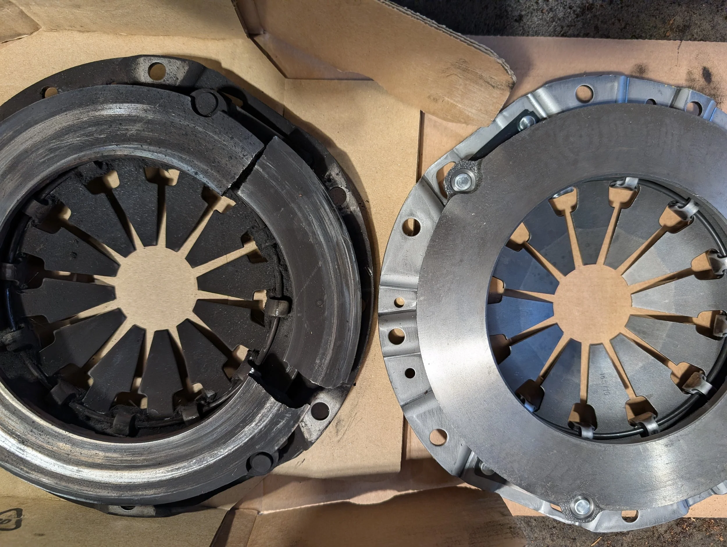 Two circular metallic clutch pressure plates placed on a cardboard surface.