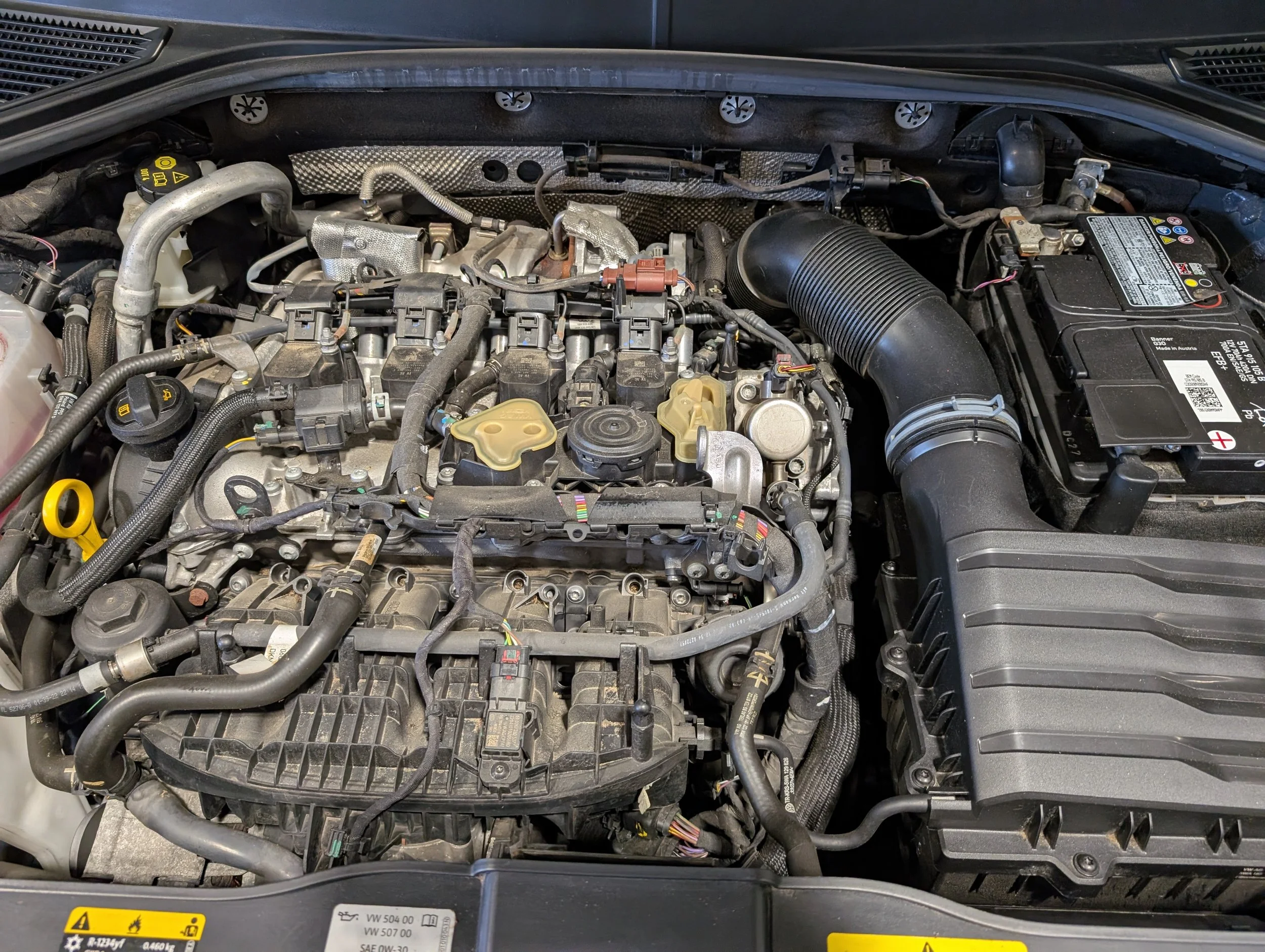 Under the hood of a vehicle showing an engine compartment with various mechanical parts, hoses, and electrical components.