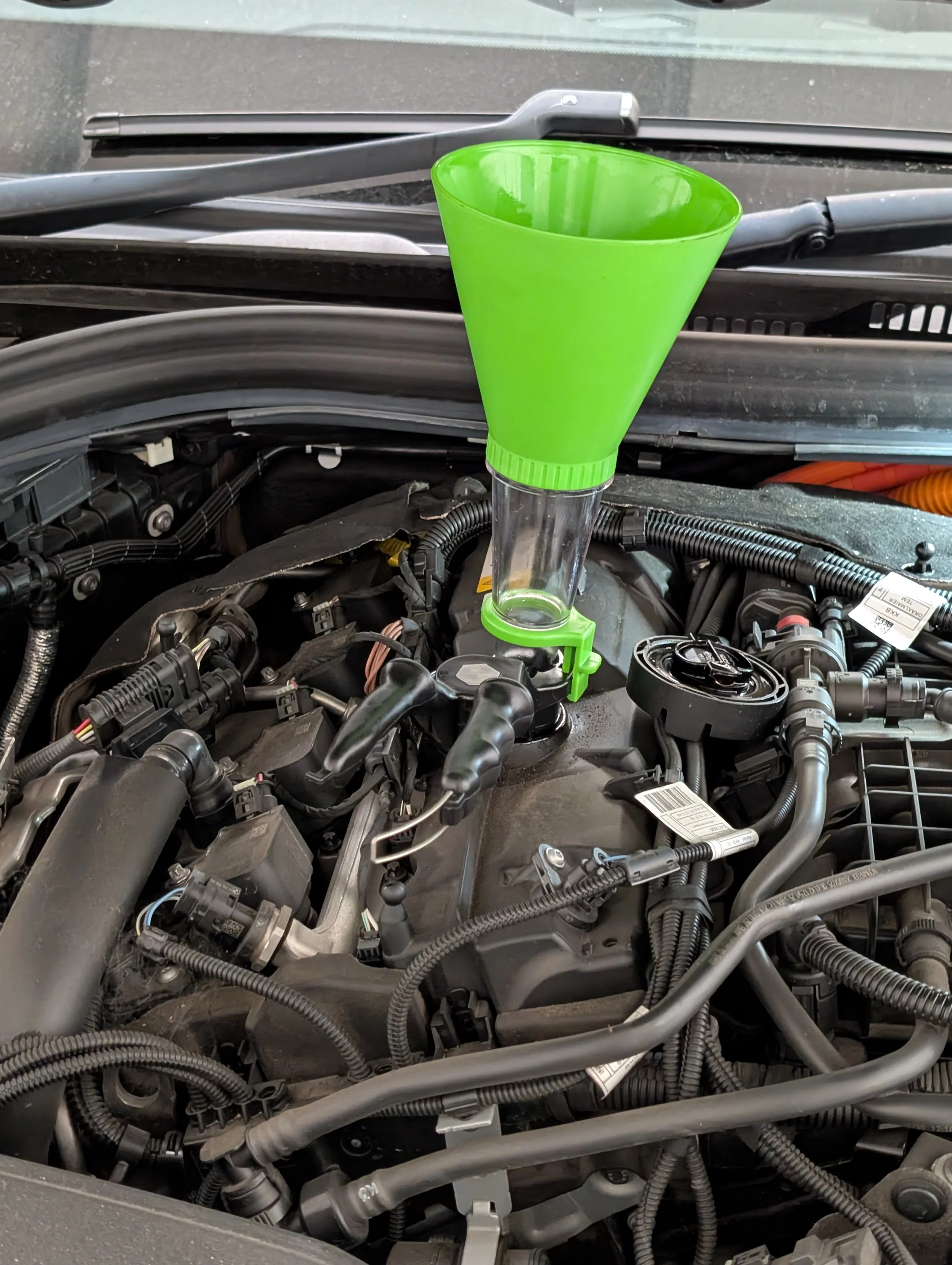 Green funnel placed inside an open car hood.