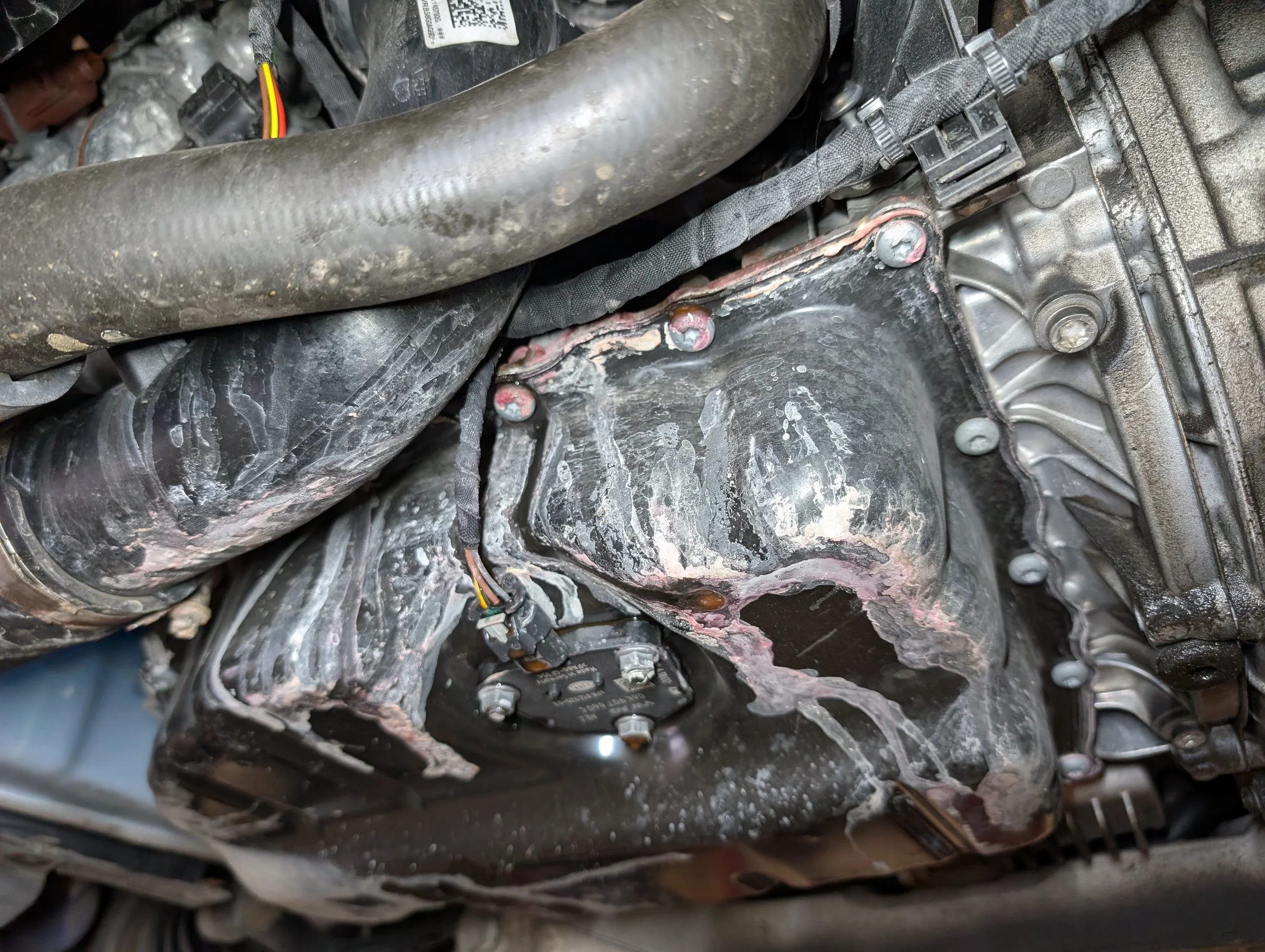 Close-up of an engine component showing oil and dirt, with bolts and wires.