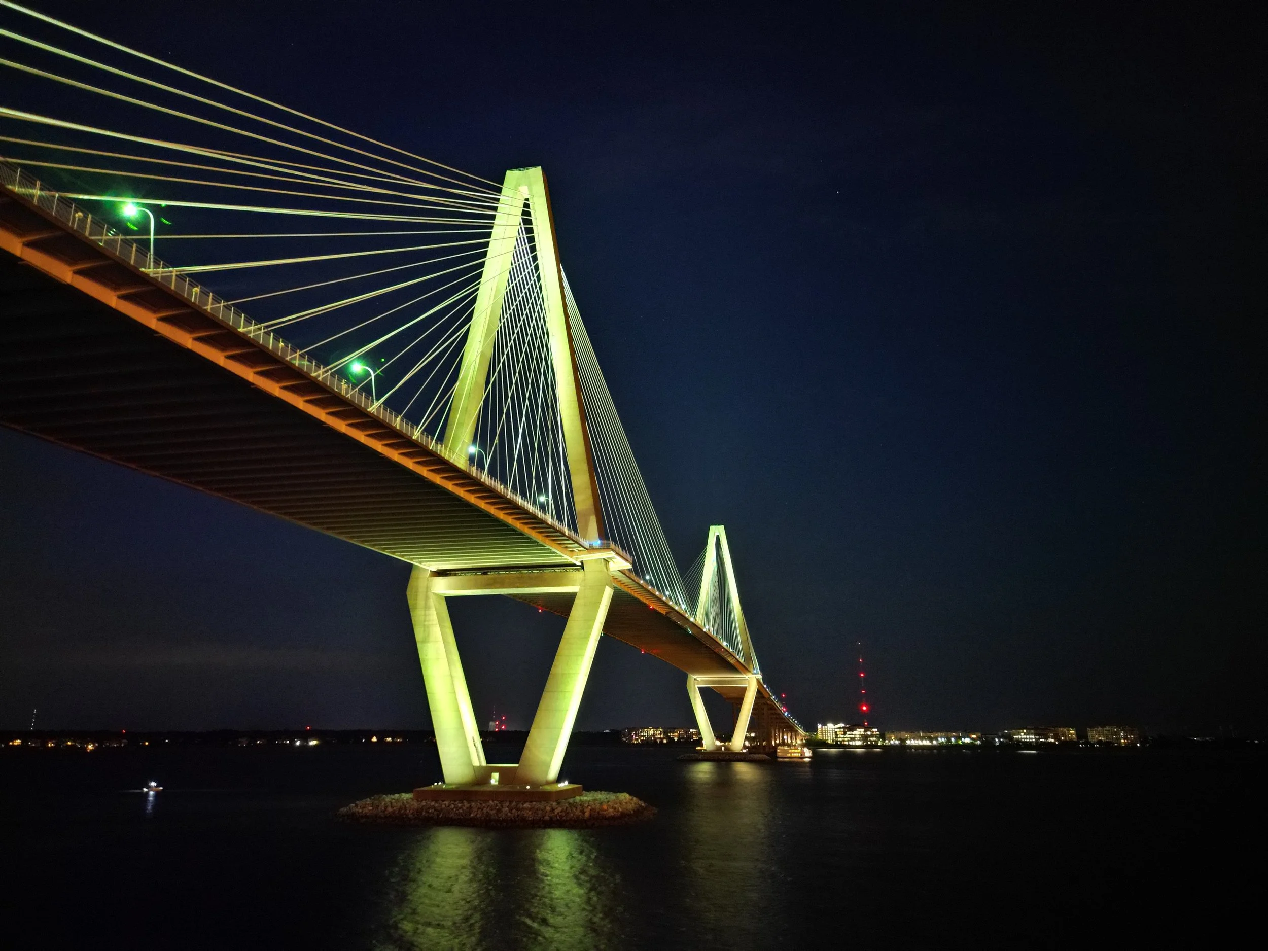 Nighttime aerial view of the illuminated Ravenel Bridge spanning Charleston Harbor.