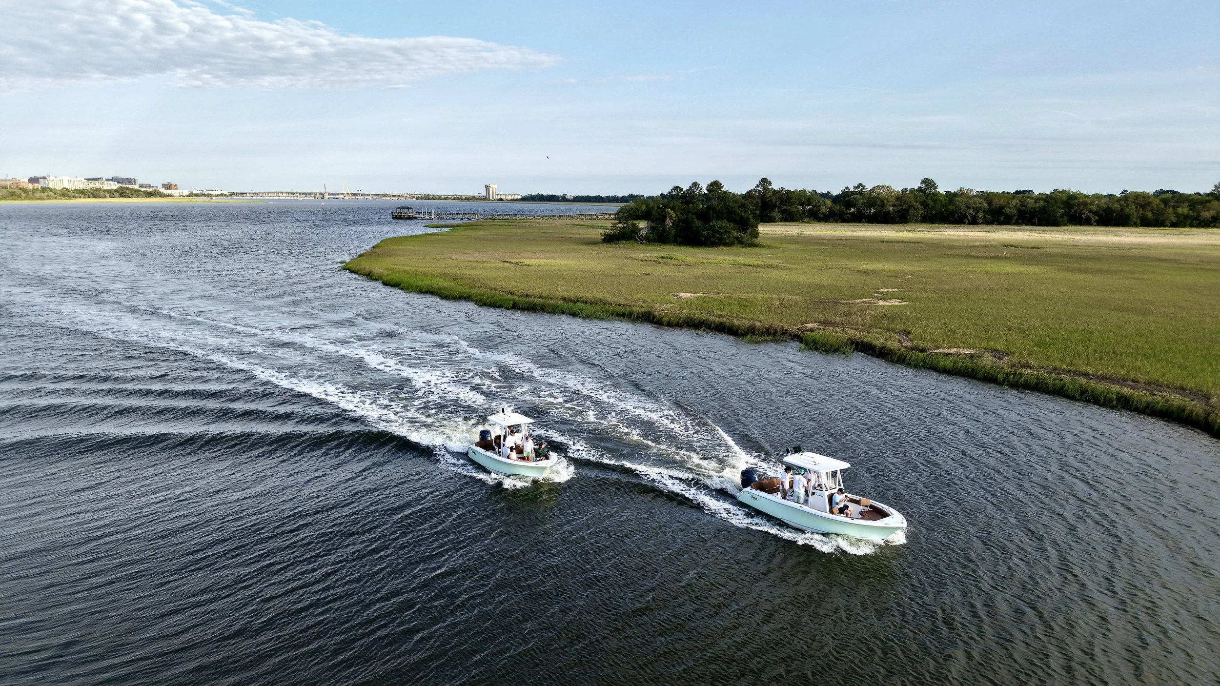 Two motorboats traveling through a marsh-lined waterway, photographed from above.