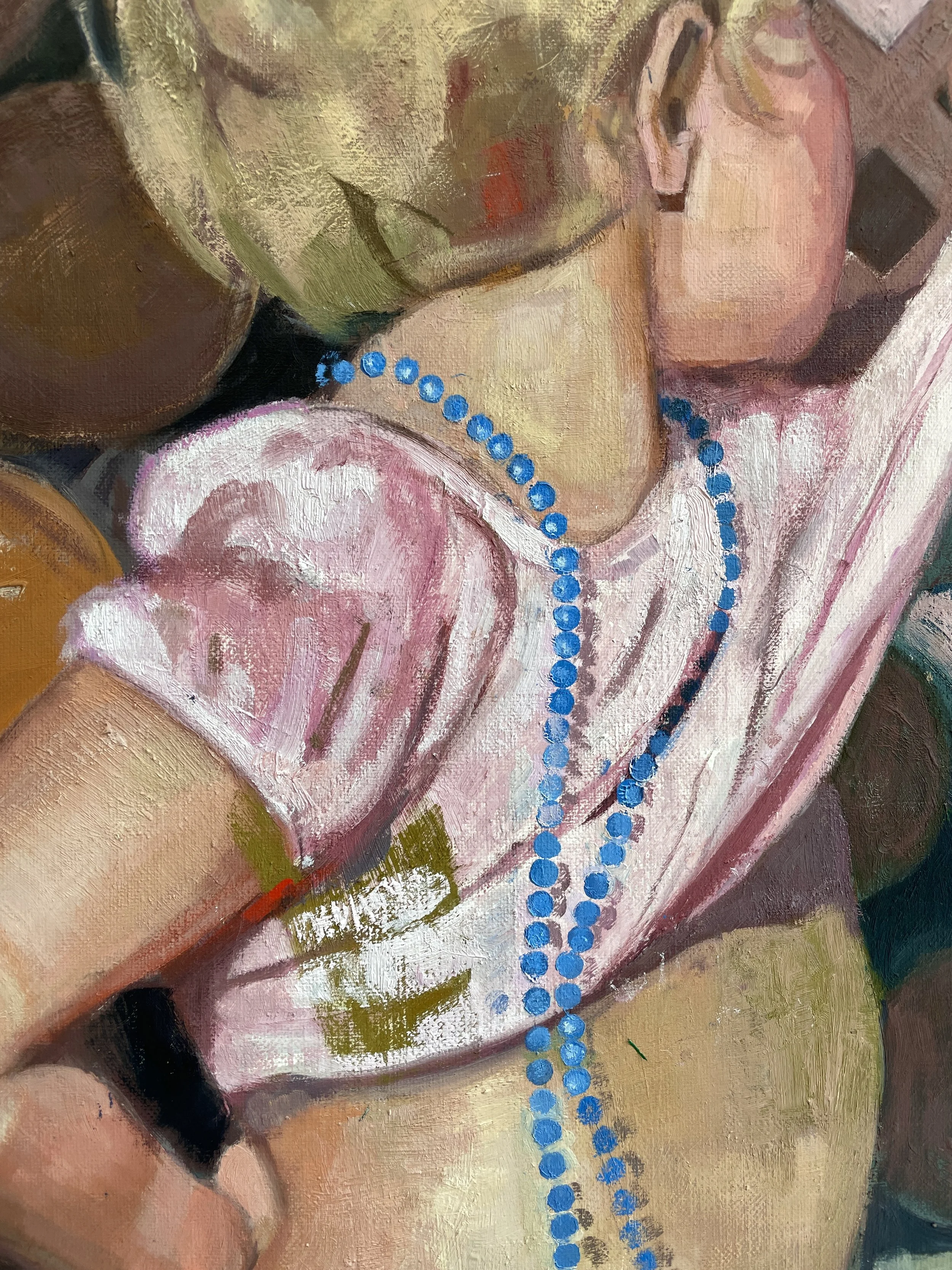 Close-up of a painted child wearing a pink shirt and a bright blue beaded necklace, with one arm raised.