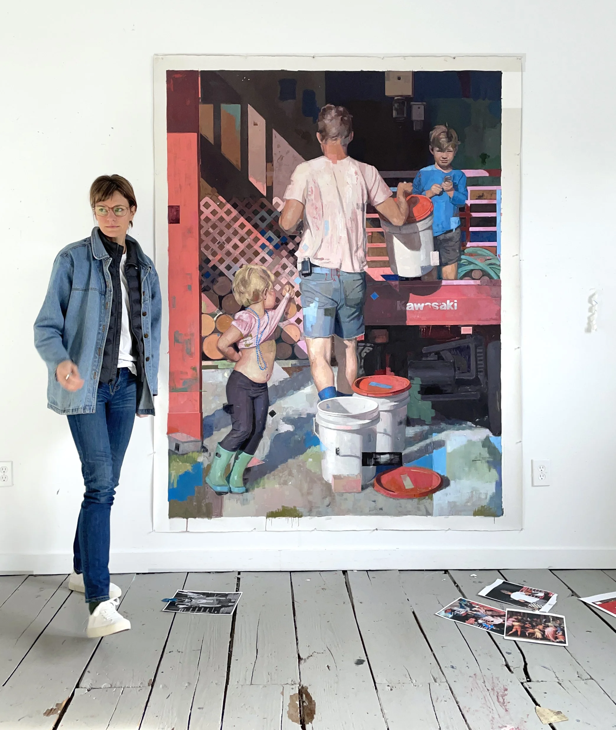 Caitlin Winner standing beside her large painting Favorite Son, which shows an adult and two children near a utility vehicle and several buckets.