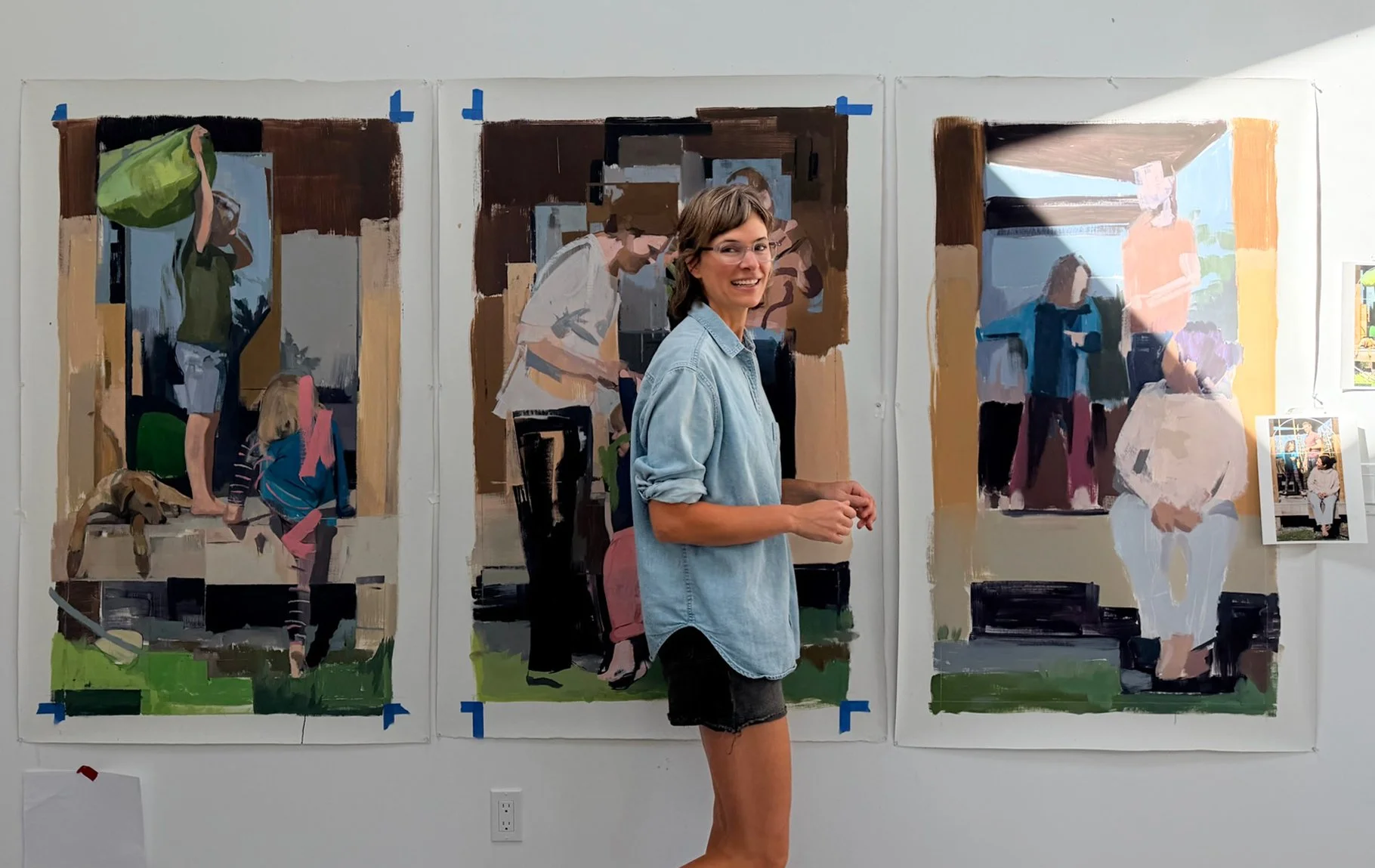Caitlin Winner smiling in front of three of her narrative paintings.