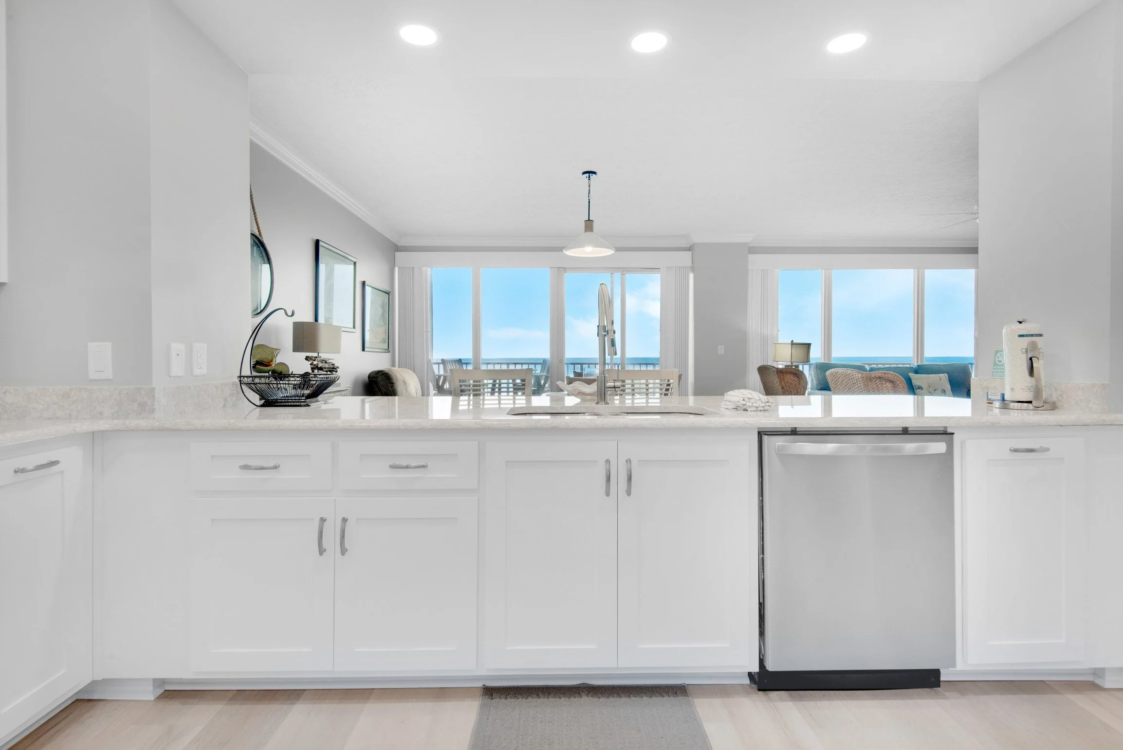 Kitchen with white cabinets and a view of a living room and balcony with large windows and ocean view.