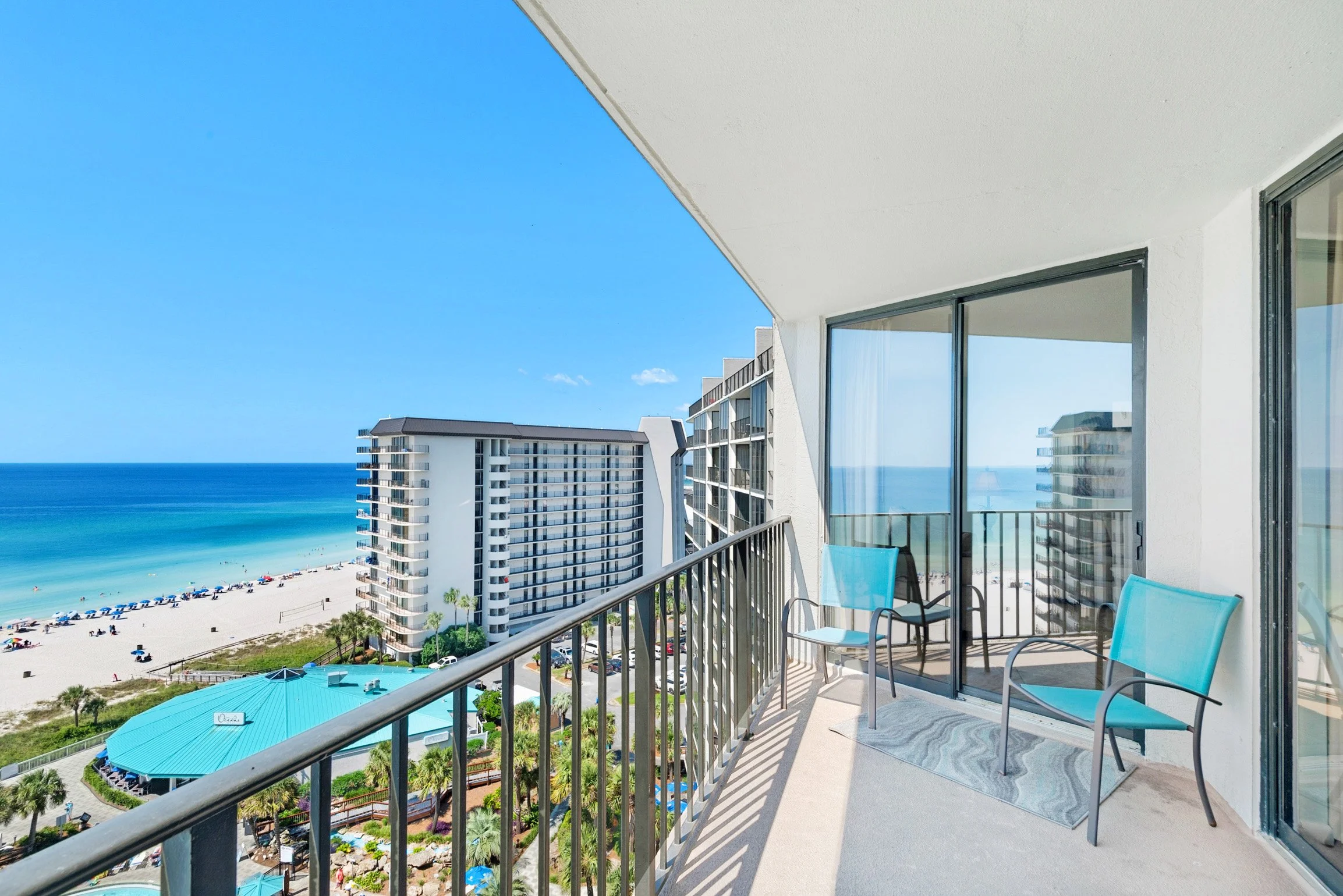 Balcony view overlooking a beach with umbrellas, and high-rise buildings under a clear blue sky.