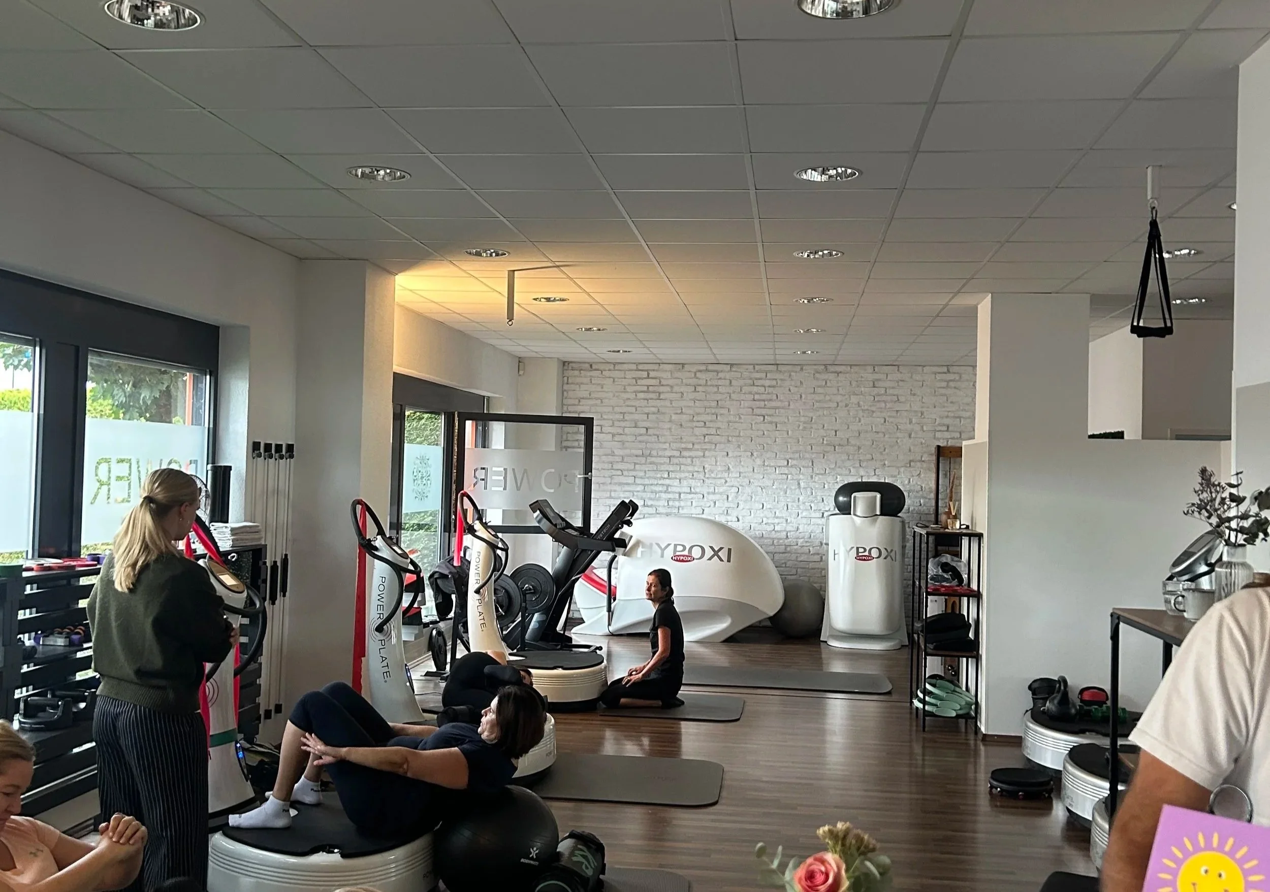 Menschen trainieren in einem Fitnessstudio mit Fitnessgeräten, Yoga-Übungen und einer Person, die auf einem Balance-Board steht.