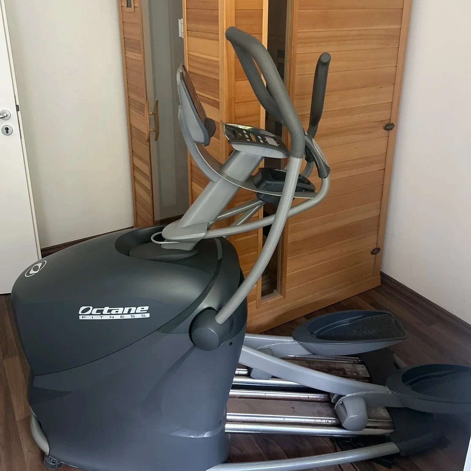Ein Laufband im Innenraum, umgeben von Holzregalen mit geschlossenen Türen, auf dunklem Holzboden.