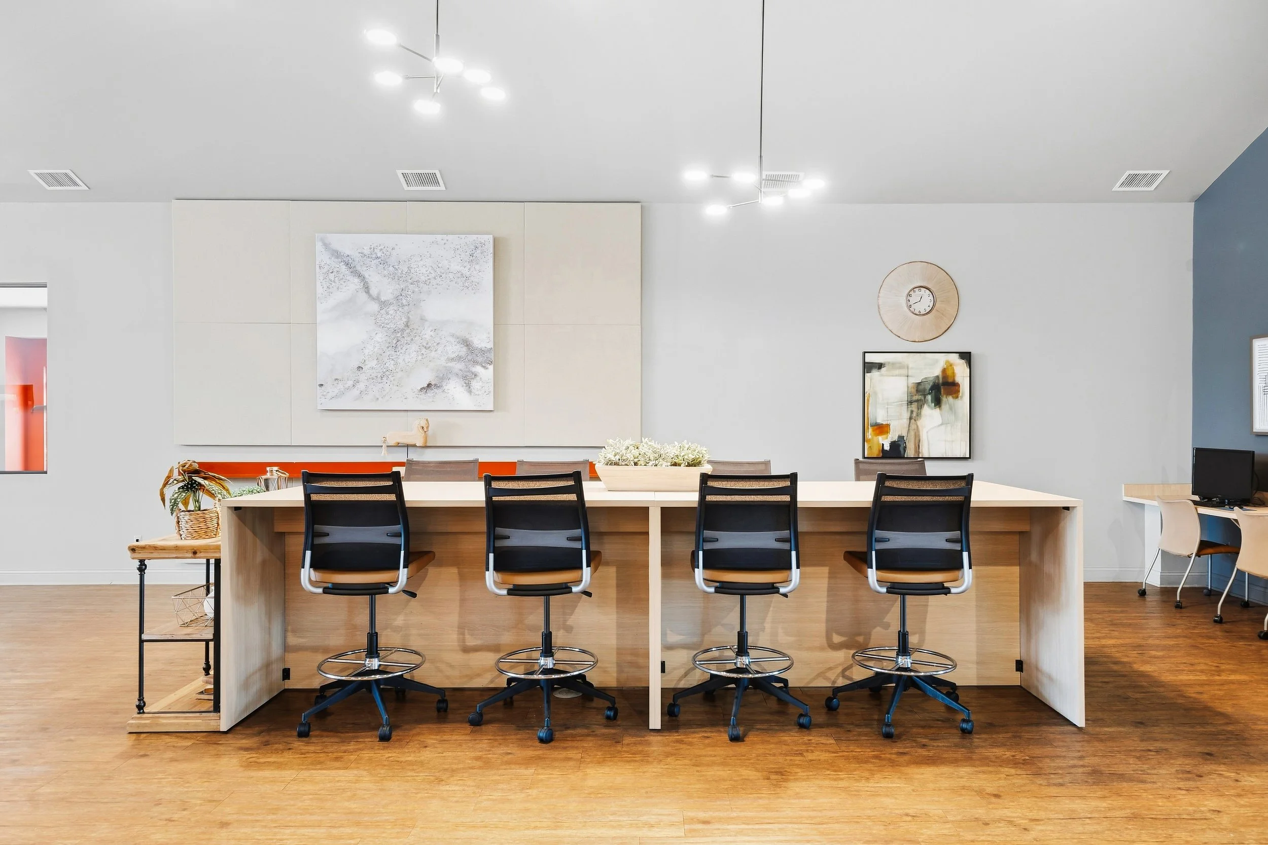 Modern conference room with a large wooden table, six black and tan chairs, wall art, a decorative plant, and a clock on the wall.